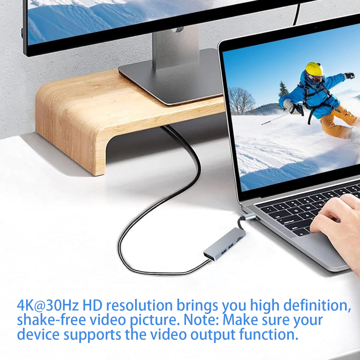 Laptop mit Monitor verbunden, zeigt Skifahrer im Schnee. Ein USB-Hub und Kabel sind ebenfalls sichtbar.