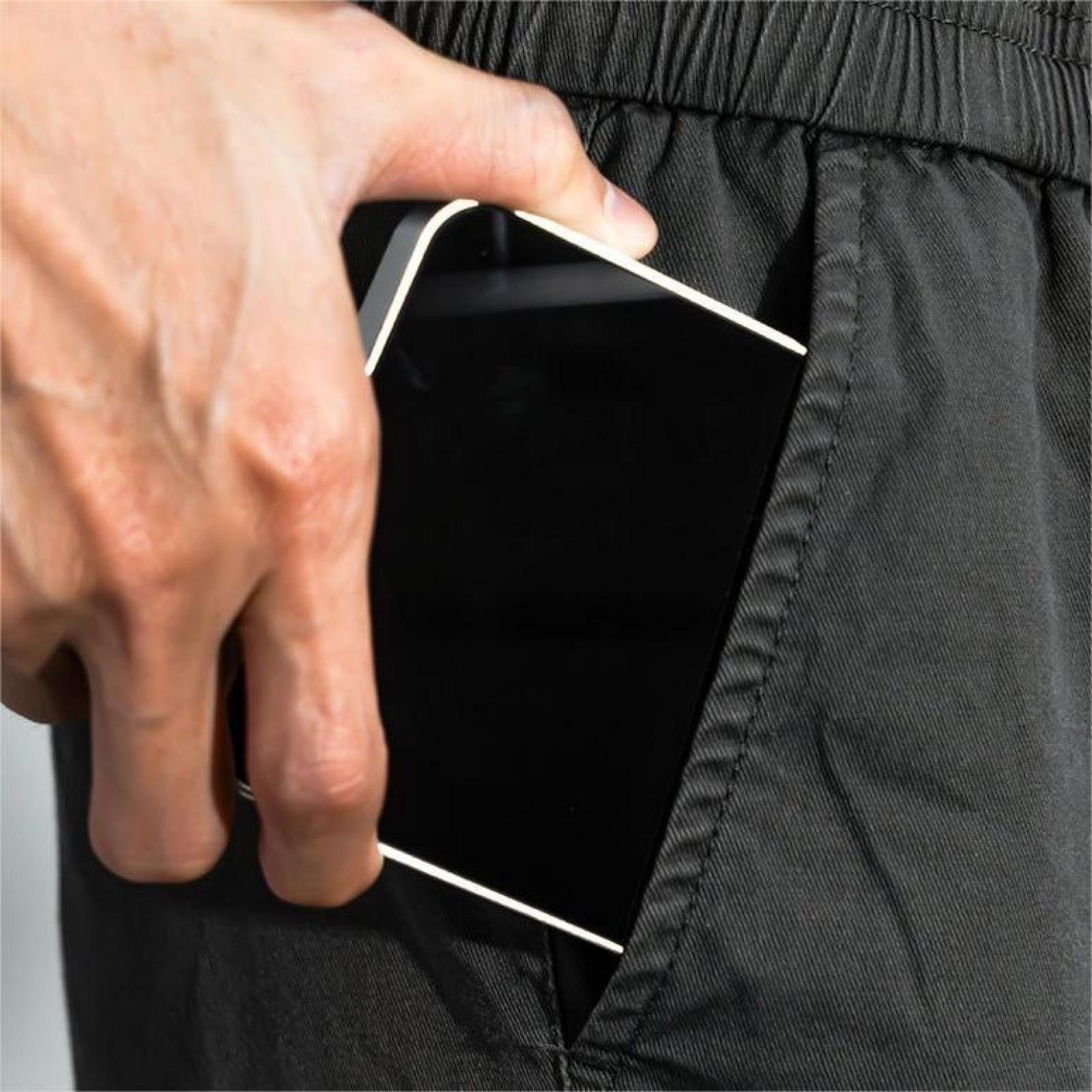 Eine Hand steckt ein schwarzes Smartphone in eine dunkelgraue Tasche. Die Tasche befindet sich auf dunkelgrauem Stoff.