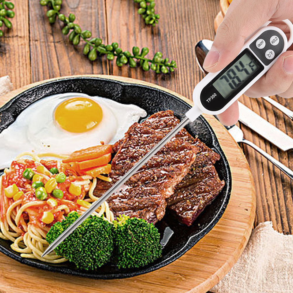 Eine Hand hält ein Lebensmitteltemperaturmessgerät und misst Steak auf einer brutzelnden Platte mit Ei, Pasta und Brokkoli. Das Thermometer zeigt 78,4°F an.