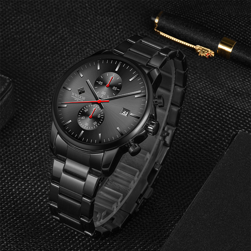 Eine schwarze Armbanduhr mit dunkelgrauem Zifferblatt, roten Akzenten und Metallband. Die Uhr liegt auf schwarzem Untergrund.