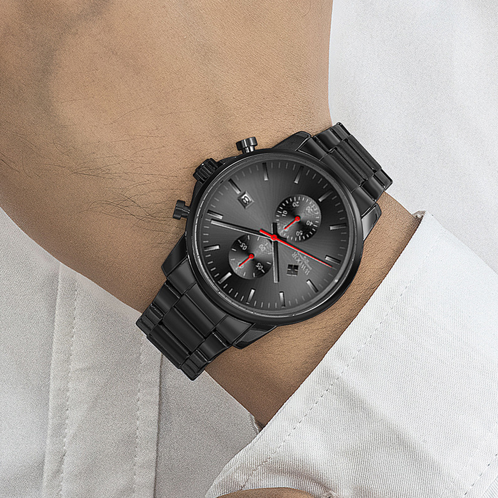 Am Handgelenk einer Person befindet sich eine schwarze Armbanduhr. Die Uhr hat ein graues Zifferblatt mit roten Akzenten. Die Person trägt ein weißes Hemd.