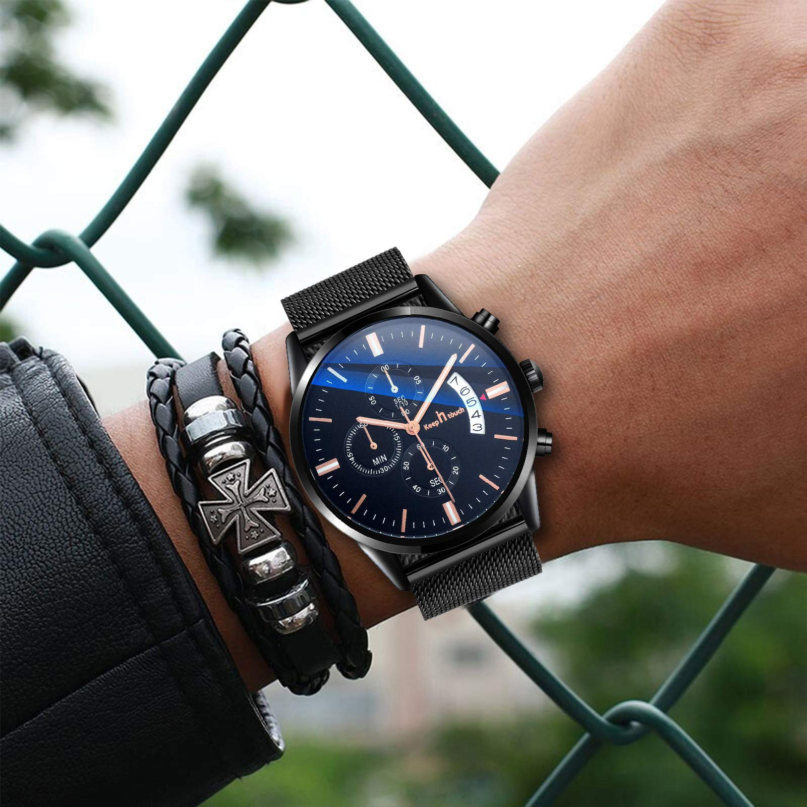 Handgelenk mit schwarzer Uhr und Lederarmband mit Kreuzdesign. Die Uhr hat ein dunkelblaues Zifferblatt.