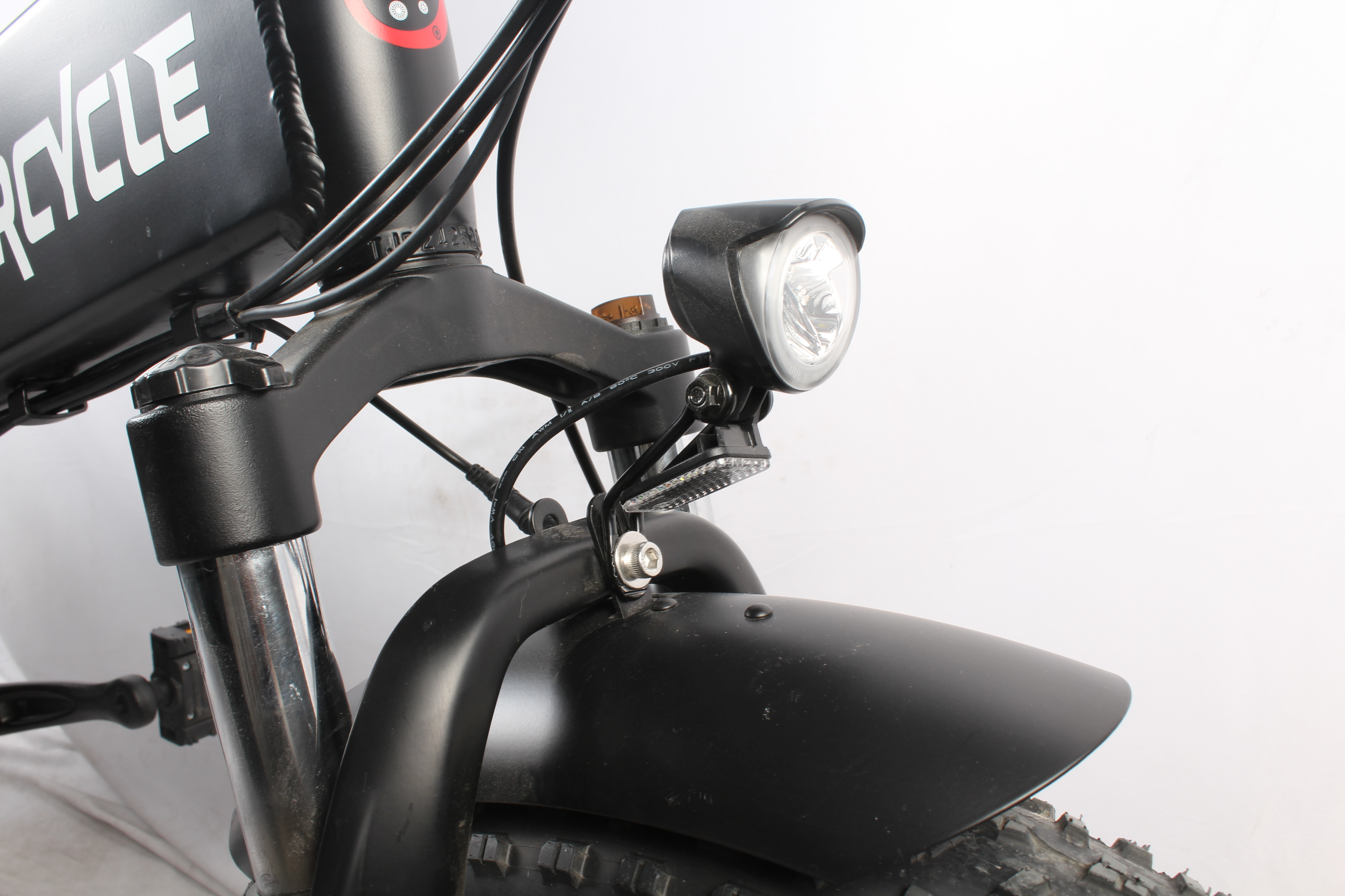 Parte anteriore della bici elettrica nera con faro, parafango e pneumatico. Il telaio è nero, con testo bianco. Lo sfondo è bianco.