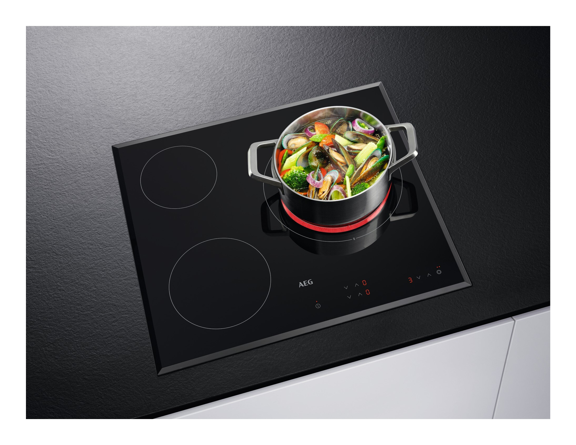 Un piano cottura a induzione nero con una pentola di cozze e verdure, il piano cottura è su una superficie nera.