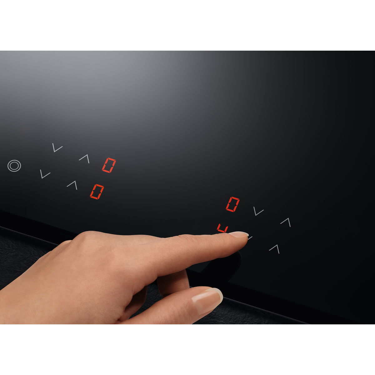 Una mano tocca un piano cottura in vetro nero. Cifre rosse mostrano '0' e '4'. Sono visibili anche i comandi touch con frecce.