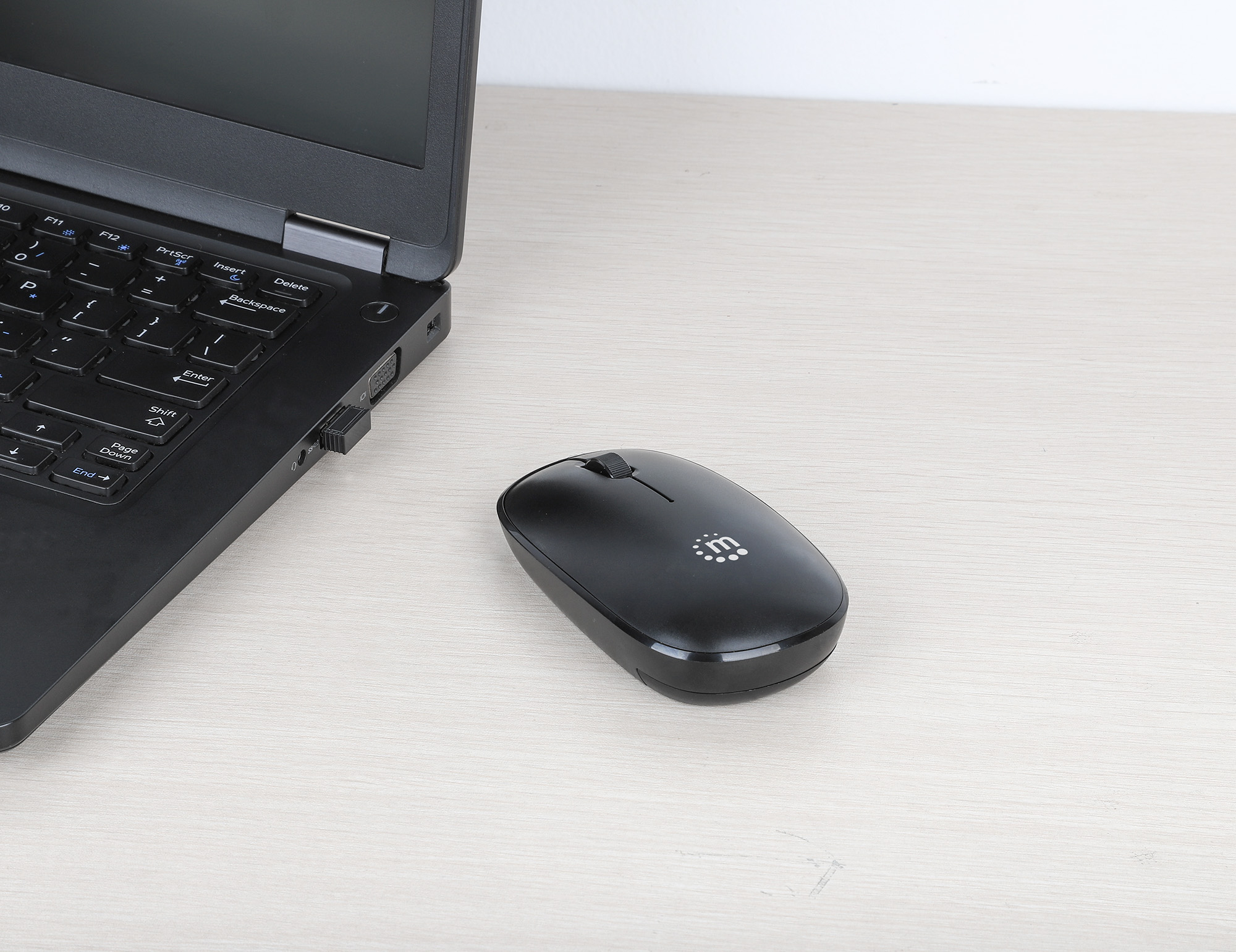 Un laptop nero è accanto a un mouse wireless nero su una superficie di legno chiaro. Il mouse ha un logo.