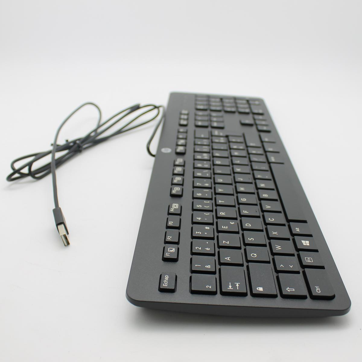 Una tastiera per computer nera con un cavo USB. La tastiera è su una superficie bianca. I tasti sono etichettati con lettere e numeri.