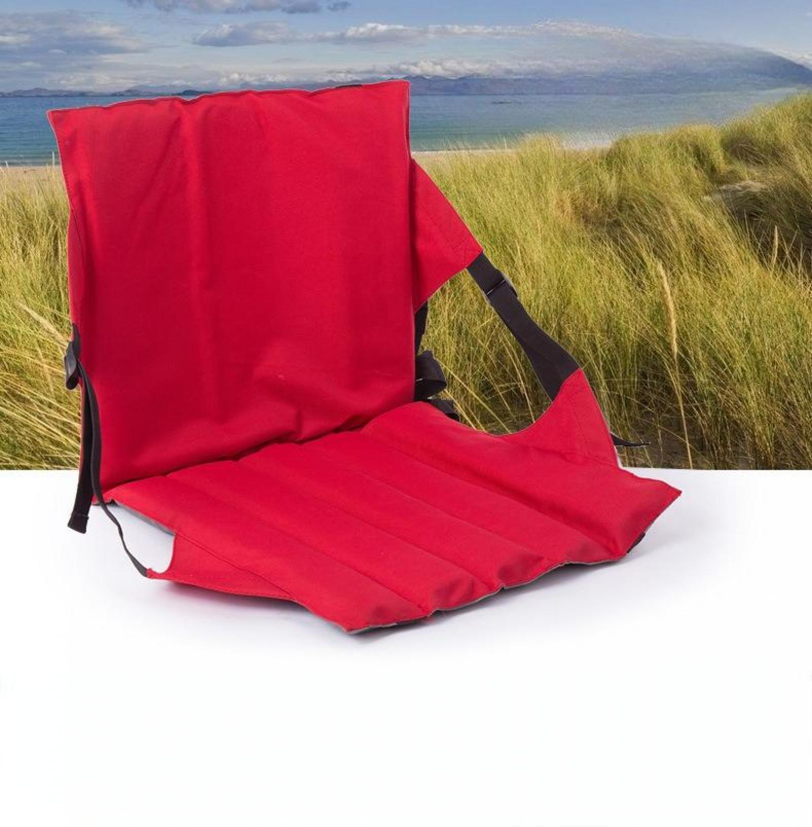 Roter Strandstuhl auf weißer Oberfläche. Hintergrund zeigt Strand, Meer und grünes Gras.