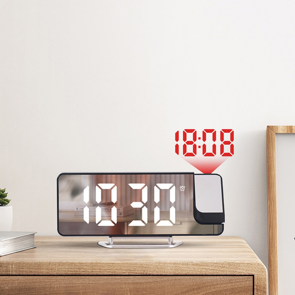 Eine Digitaluhr zeigt 10:30 auf einem Holztisch. Eine rote Projektion zeigt 18:08. Links sind eine Pflanze und ein Buch.