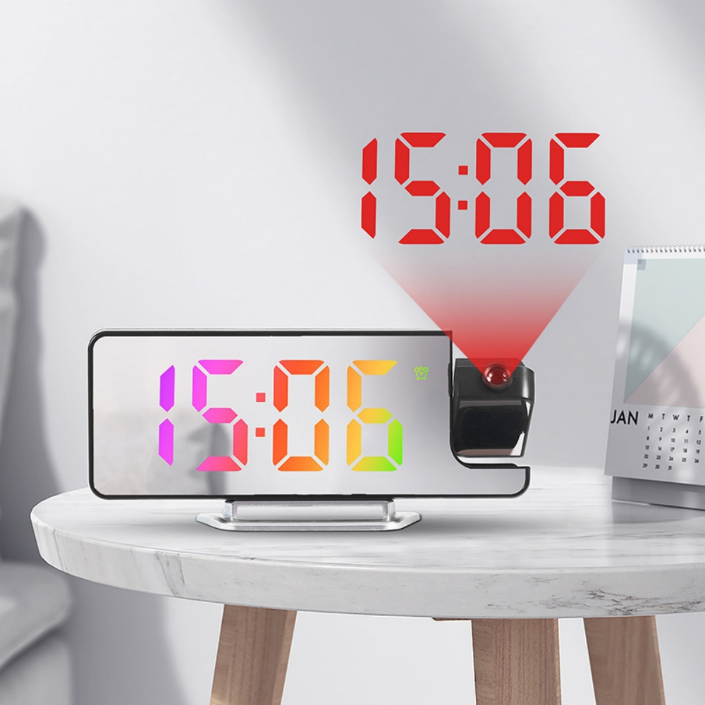 Eine Digitaluhr zeigt 15:06 in bunten Ziffern an. Ein roter Laser projiziert die Zeit auf die Wand. Die Uhr steht auf einem Tisch.