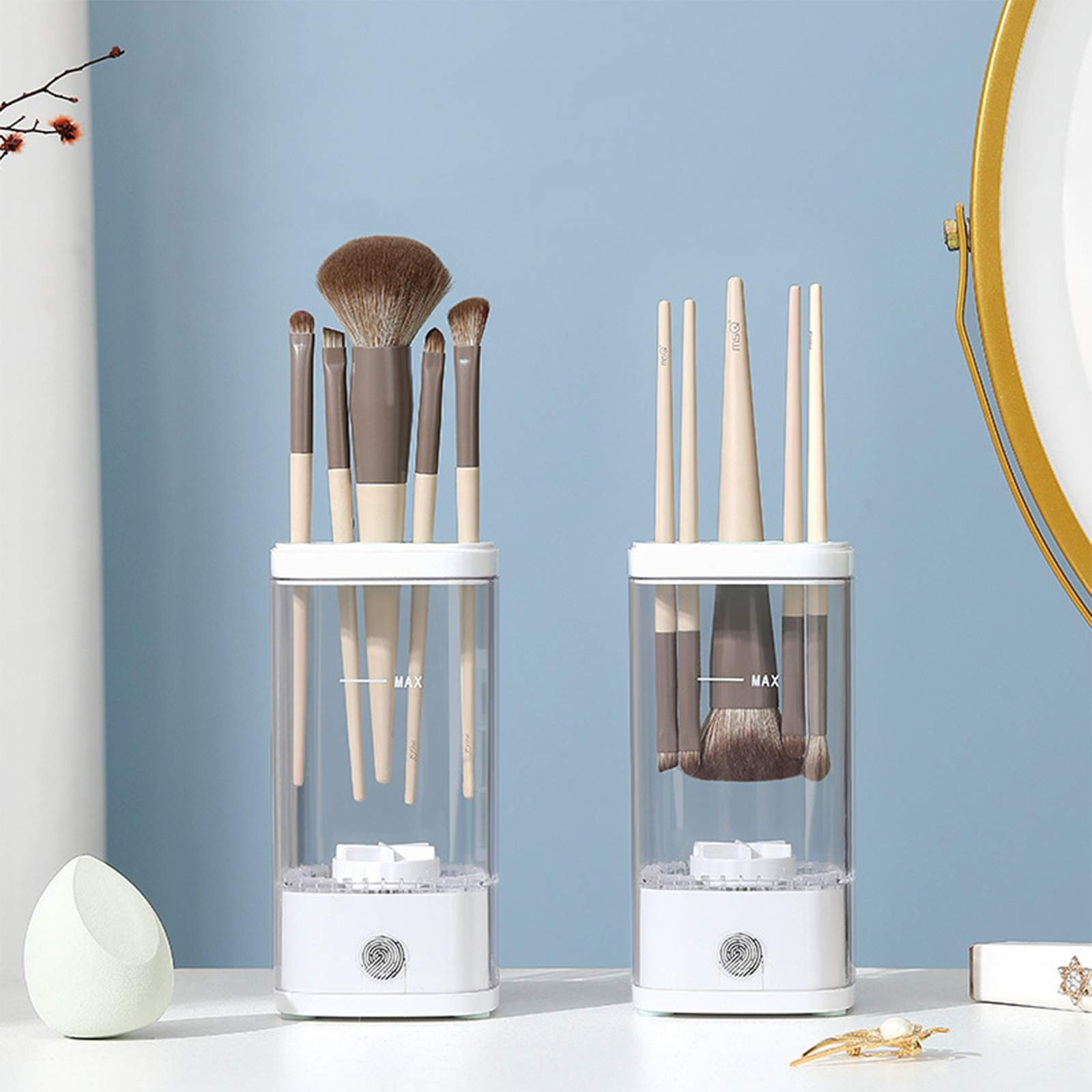 Zwei transparente Behälter mit Make-up-Pinseln. Einer hat braune Pinsel, der andere hellbeige. Blauer Hintergrund und weißer Tisch.