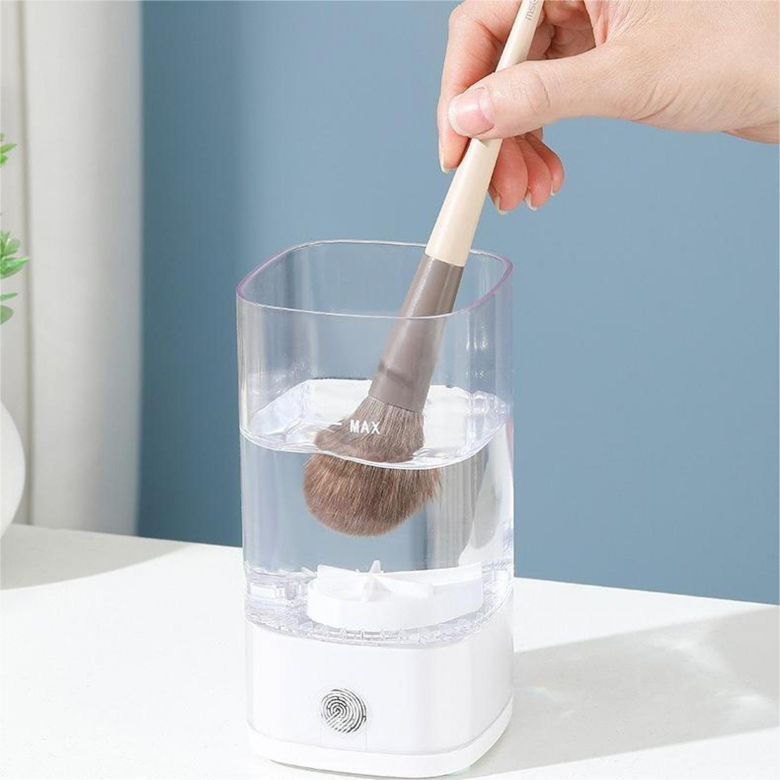 Ein Make-up-Pinsel wird in einen mit Wasser gefüllten Reiniger getaucht. Der Pinsel ist braun und der Reiniger weiß und klar.