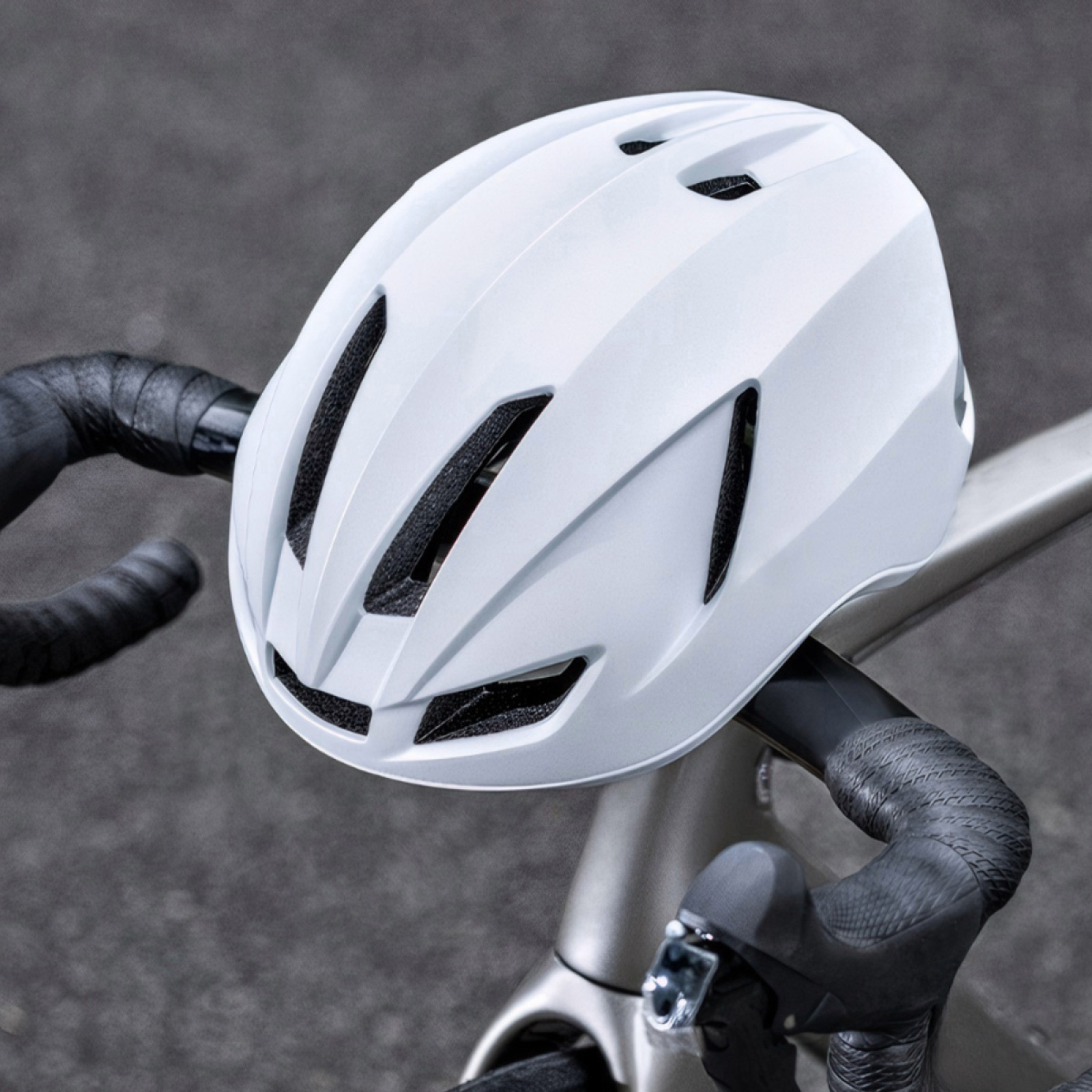 Ein weißer Fahrradhelm liegt auf einem Fahrradlenker. Der Lenker ist mit schwarzem Klebeband umwickelt. Der Hintergrund ist grau.