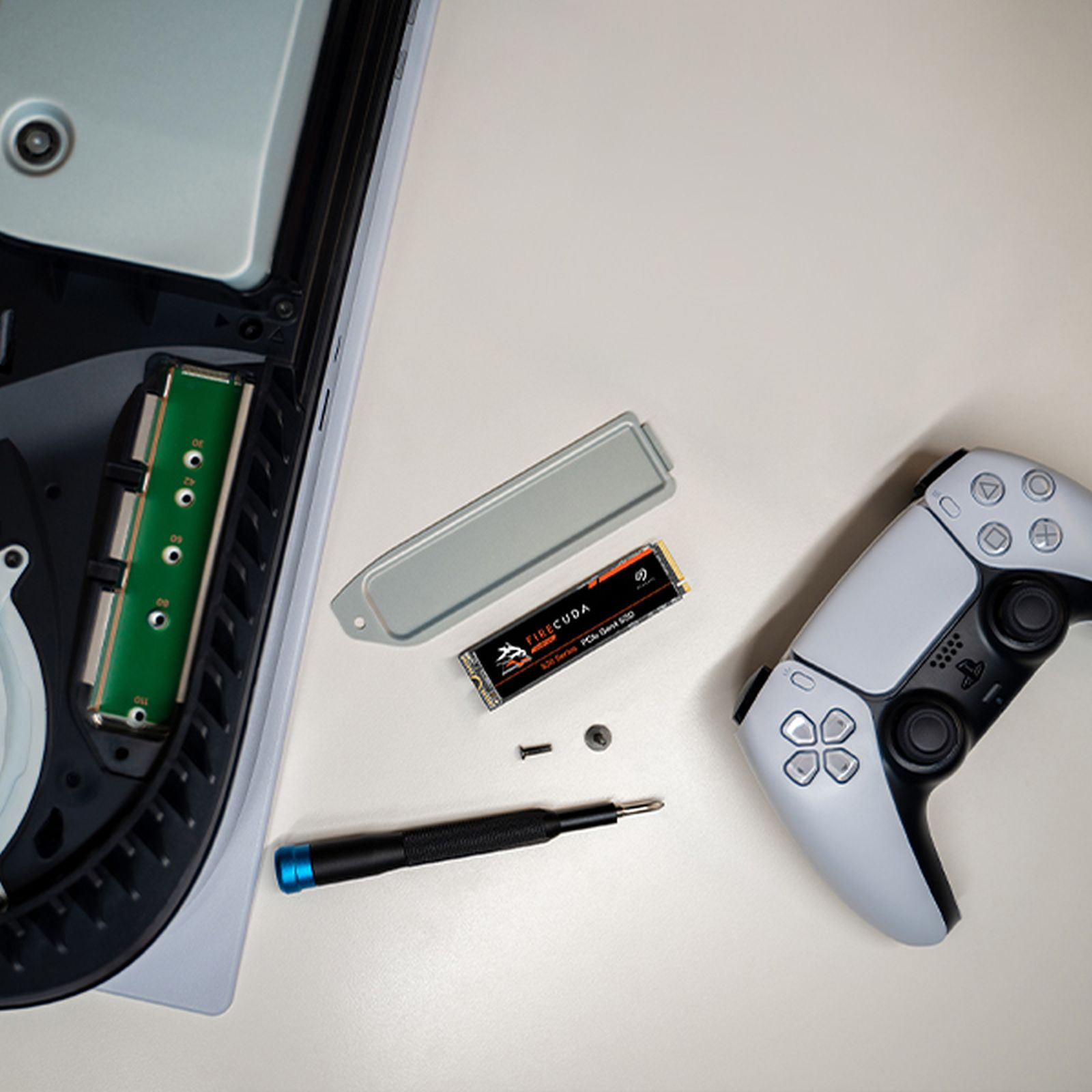 Zdemontowane PlayStation 5 z otwartą obudową, dyskiem SSD, śrubokrętem i kontrolerem na białej powierzchni.
