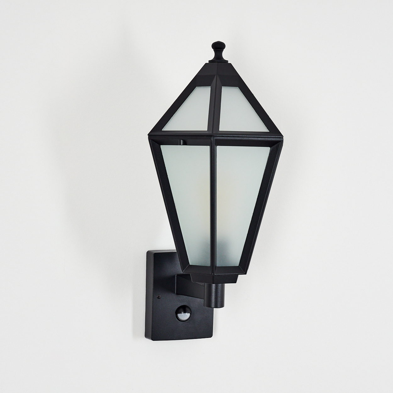Schwarze Außenwandleuchte mit Milchglasschirm, an weißer Wand befestigt. Die Lampe hat einen Bewegungssensor.