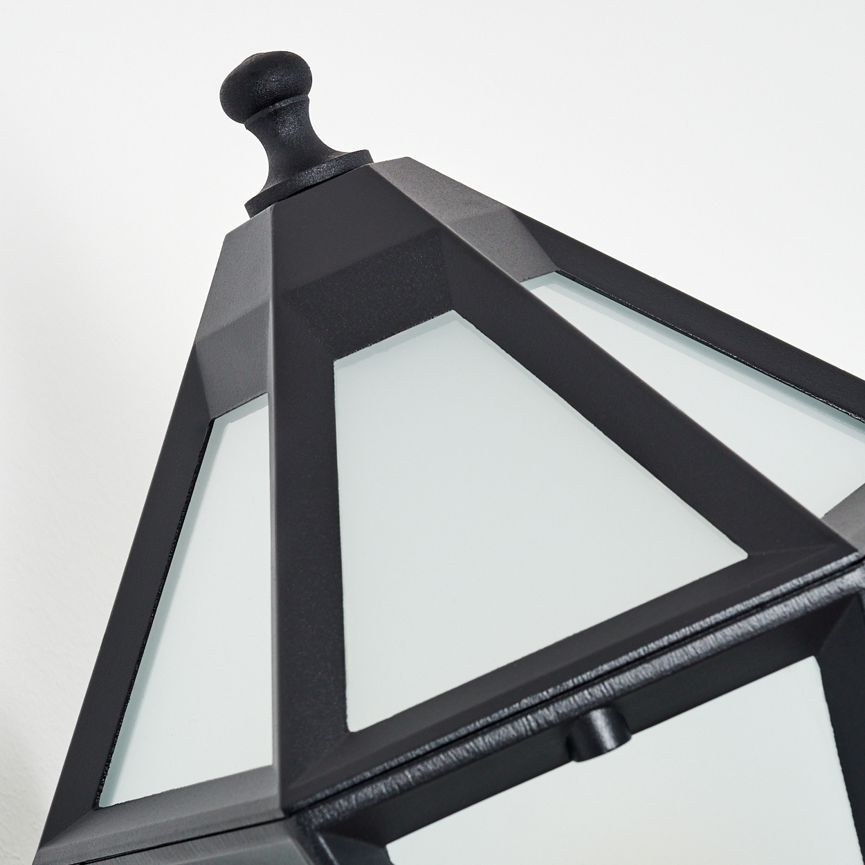 Nahaufnahme einer schwarzen, geometrischen Außenlampe vor weißem Hintergrund. Die Lampe hat Milchglasplatten.