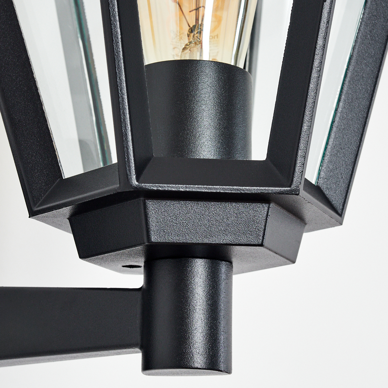 Nahaufnahme einer schwarzen Außenlampe. Sie hat ein Glasgehäuse und eine sichtbare Glühbirne. Die Lampe ist an einer schwarzen Stange befestigt.