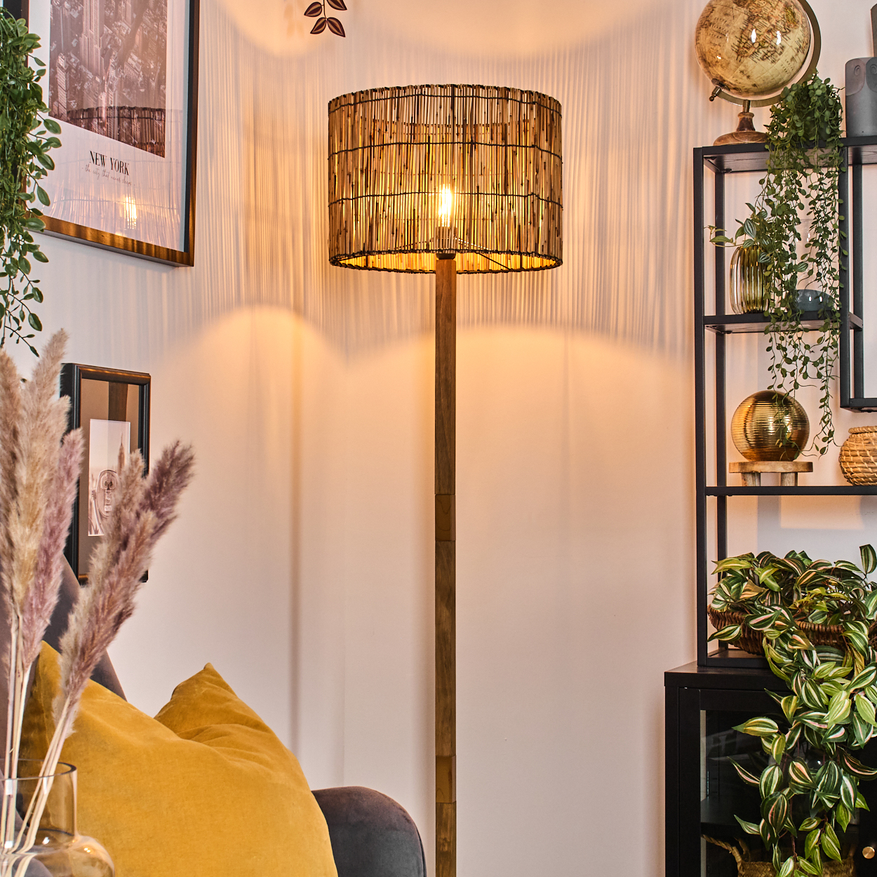 Eine beleuchtete gewebte Lampe steht in einem Raum mit Globus, Pflanzen und einem gerahmten New York-Bild. Gelbes Kissen auf einer Couch.