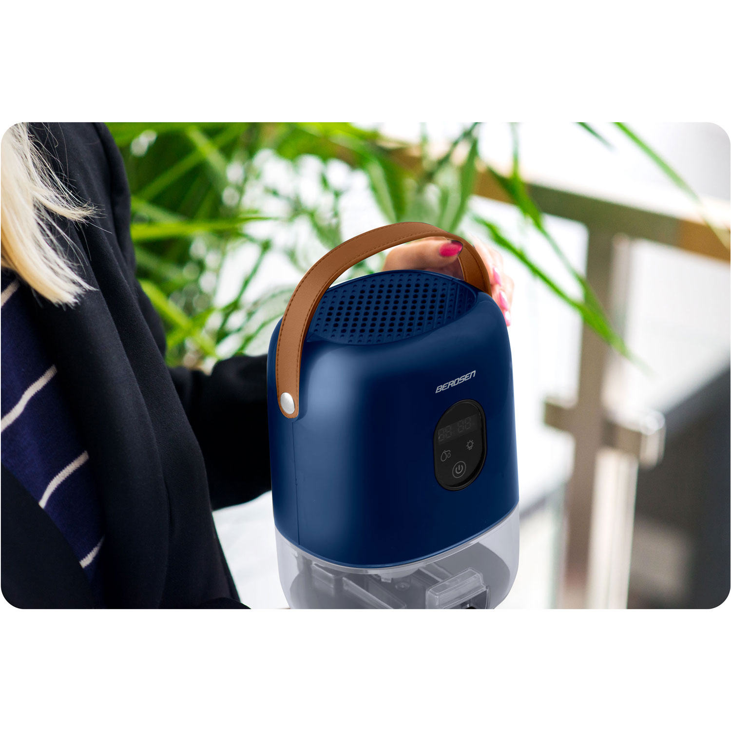 Osoba trzyma niebiesko-biały osuszacz z brązowym uchwytem. Tło obejmuje zielone liście i budynek.