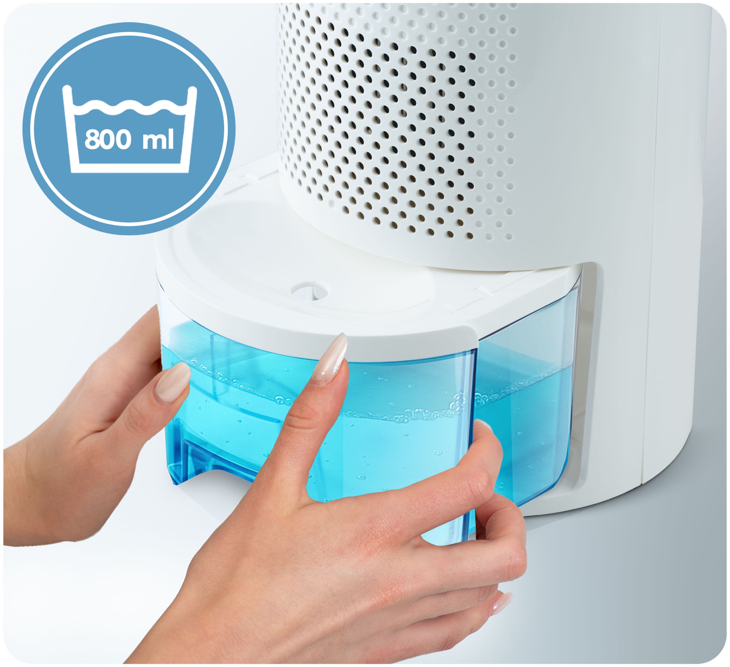 Ręce trzymają zbiornik na wodę osuszacza powietrza. Zbiornik jest wypełniony niebieską wodą. Znak pokazuje 800 ml.