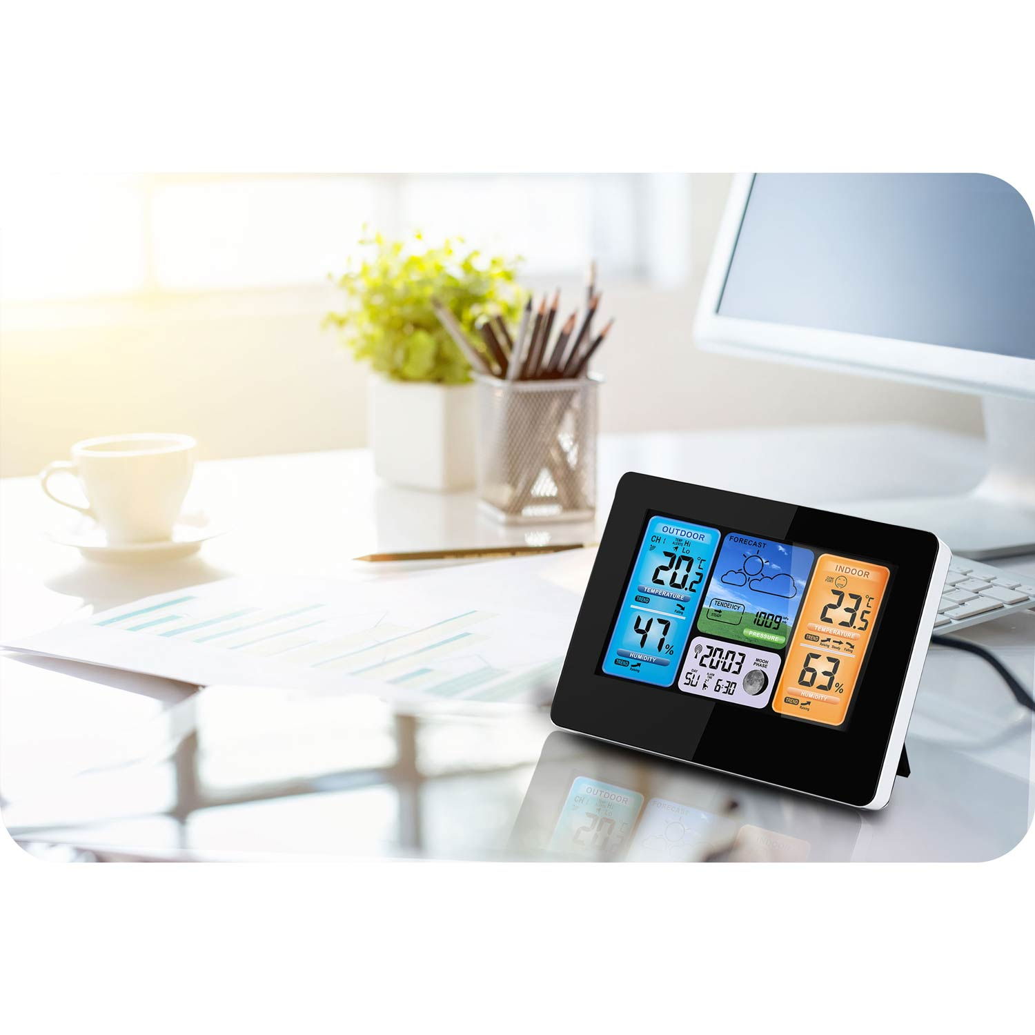 Stacja pogodowa pokazuje temperaturę zewnętrzną i wewnętrzną, wilgotność i prognozę na biurku z komputerem i kubkiem.