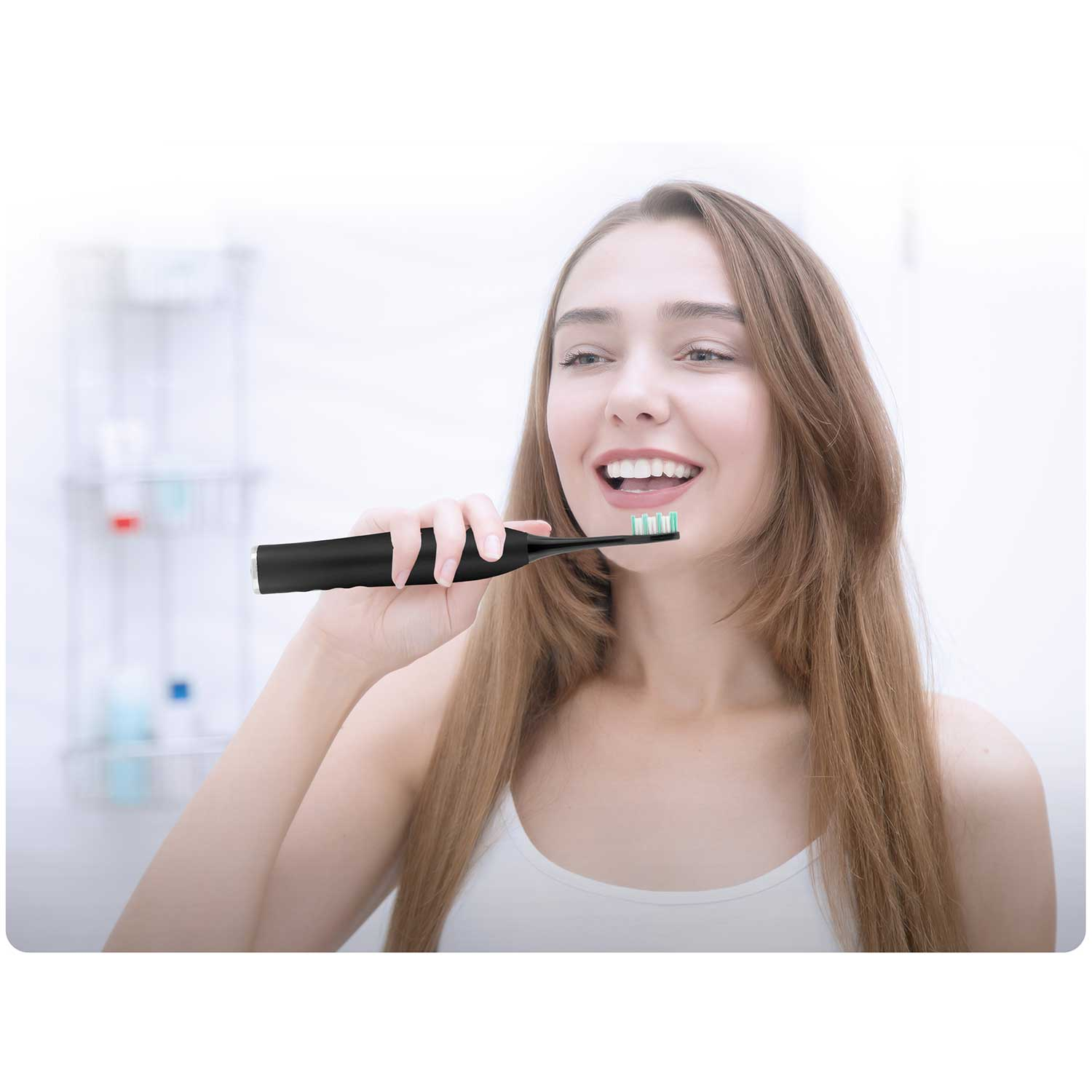 Kobieta szczotkuje zęby czarną elektryczną szczoteczką w łazience. Uśmiecha się. Tło jest rozmyte.