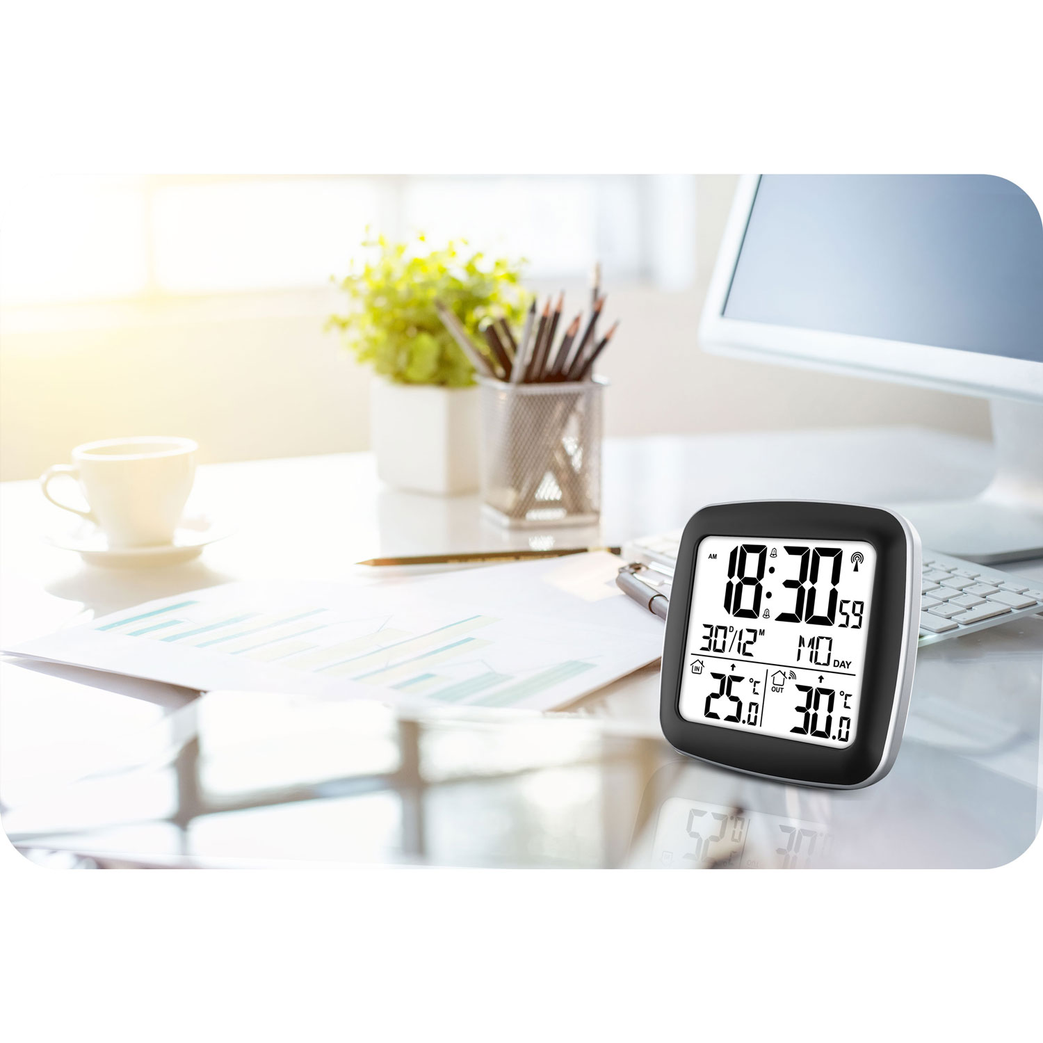 Biurko z cyfrowym zegarem pokazującym godzinę i temperaturę. Inne elementy to kubek, ołówki, komputer i papiery.