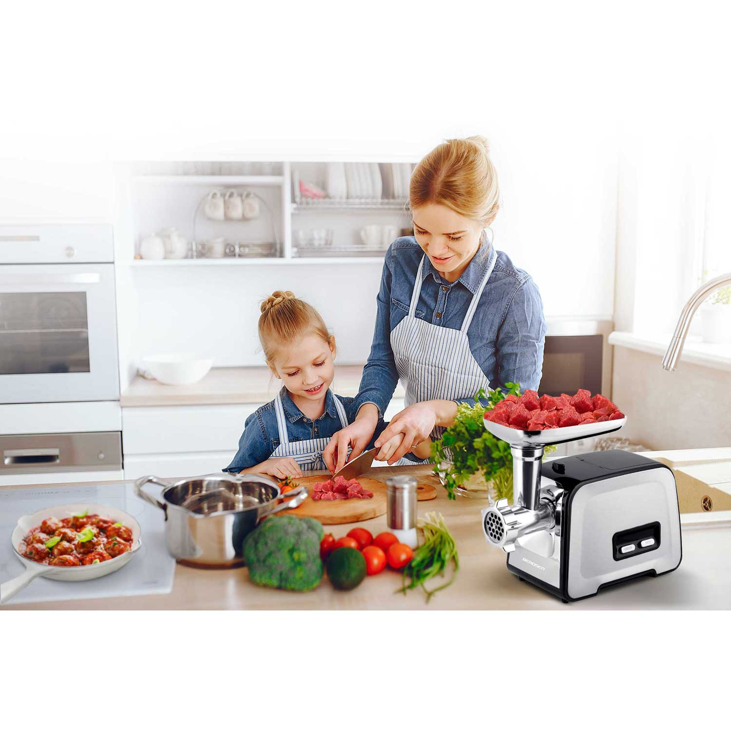 Kobieta i dziewczynka przygotowują jedzenie w kuchni. Po prawej stronie maszynka do mięsa. Warzywa i patelnia z jedzeniem z przodu.
