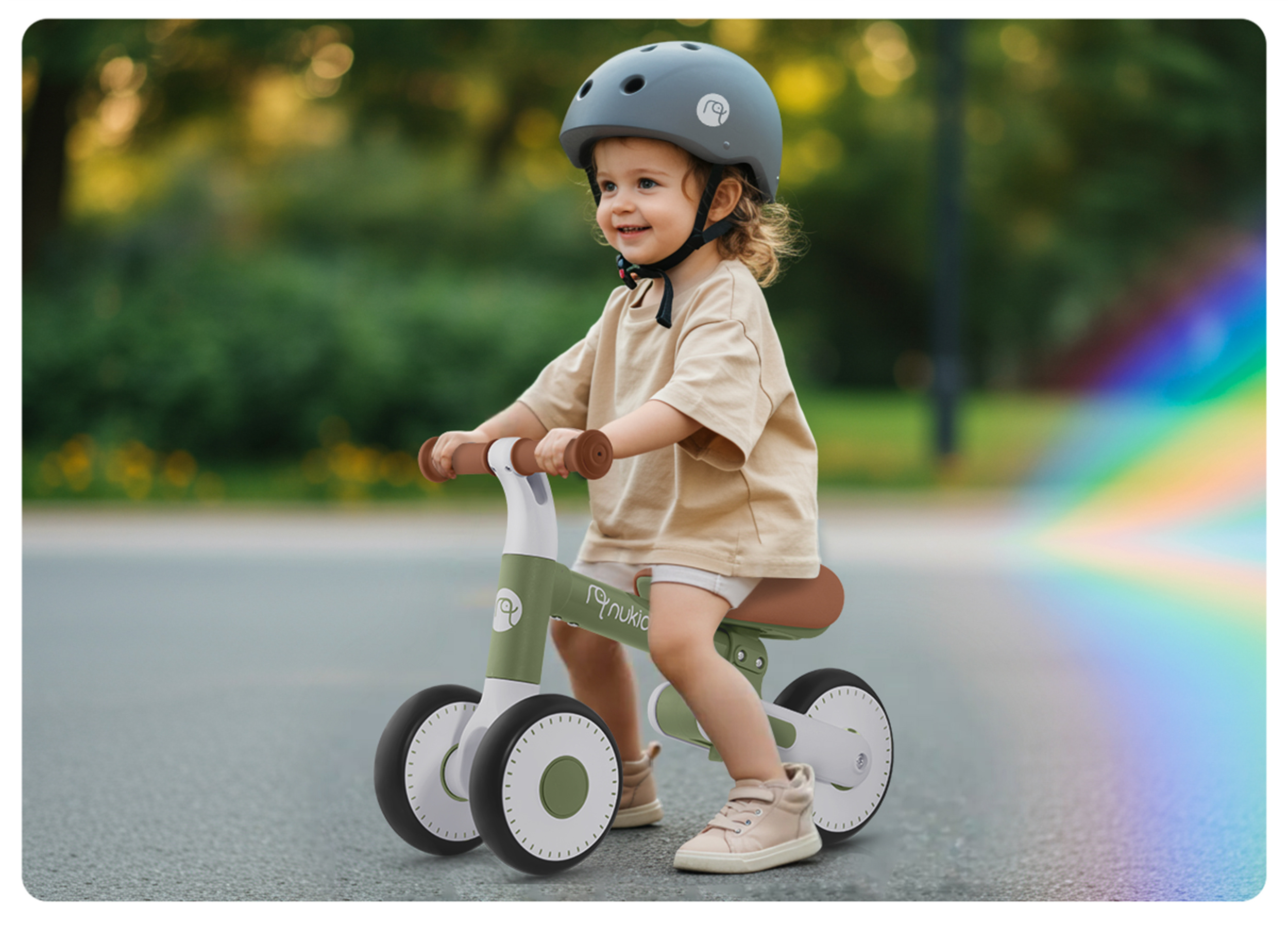 Dziecko na rowerze biegowym ma na sobie kask. Rower jest zielono-biały. Dziecko się uśmiecha.