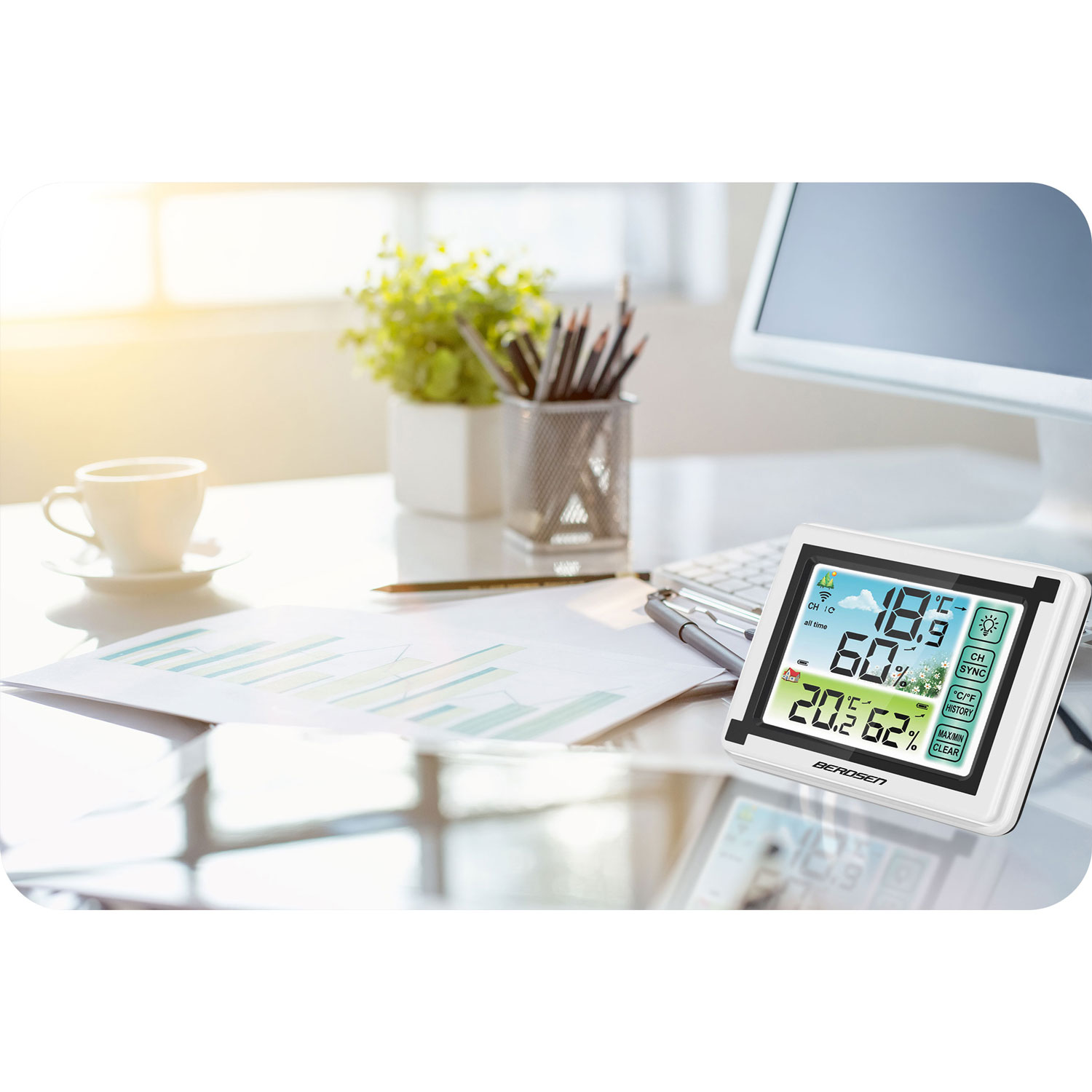 Biurko ze stacją pogodową wyświetlającą temperaturę i wilgotność. Na biurku są również filiżanka, papiery i komputer.
