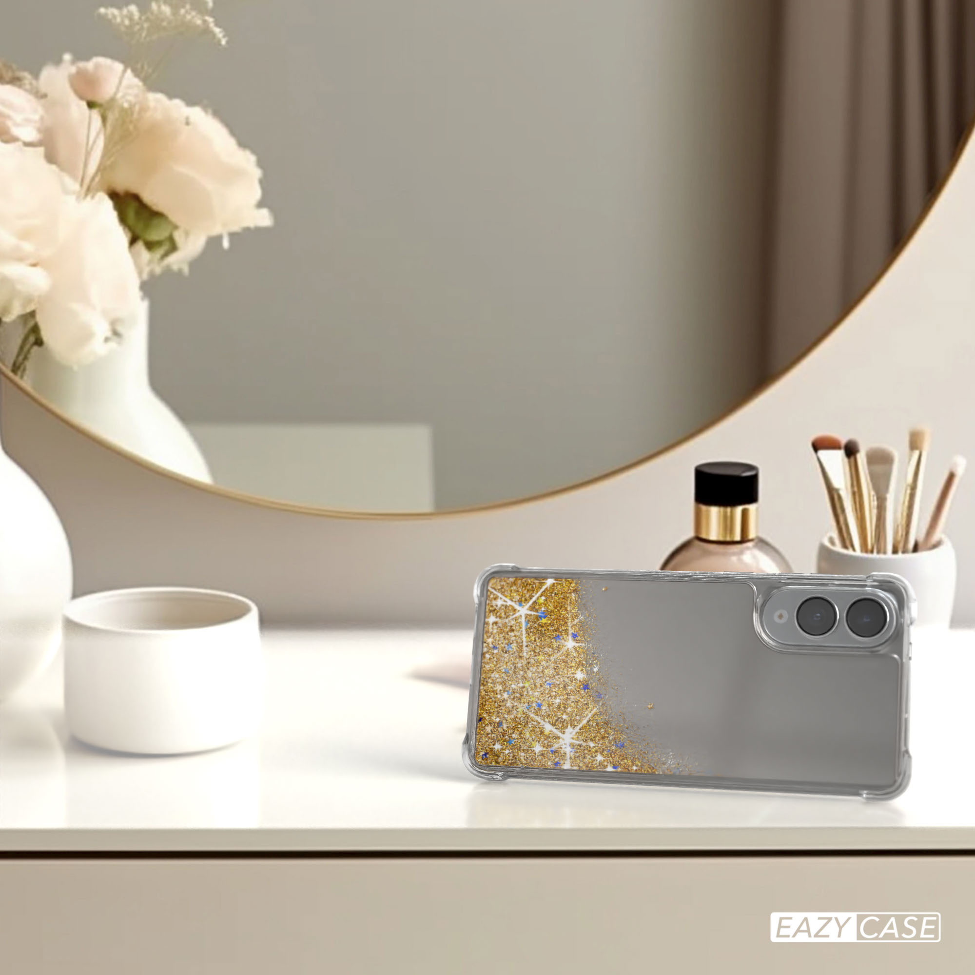 Handyhülle mit Goldglitzer auf einem weißen Tisch, Blumen in einer Vase und ein Spiegel im Hintergrund.