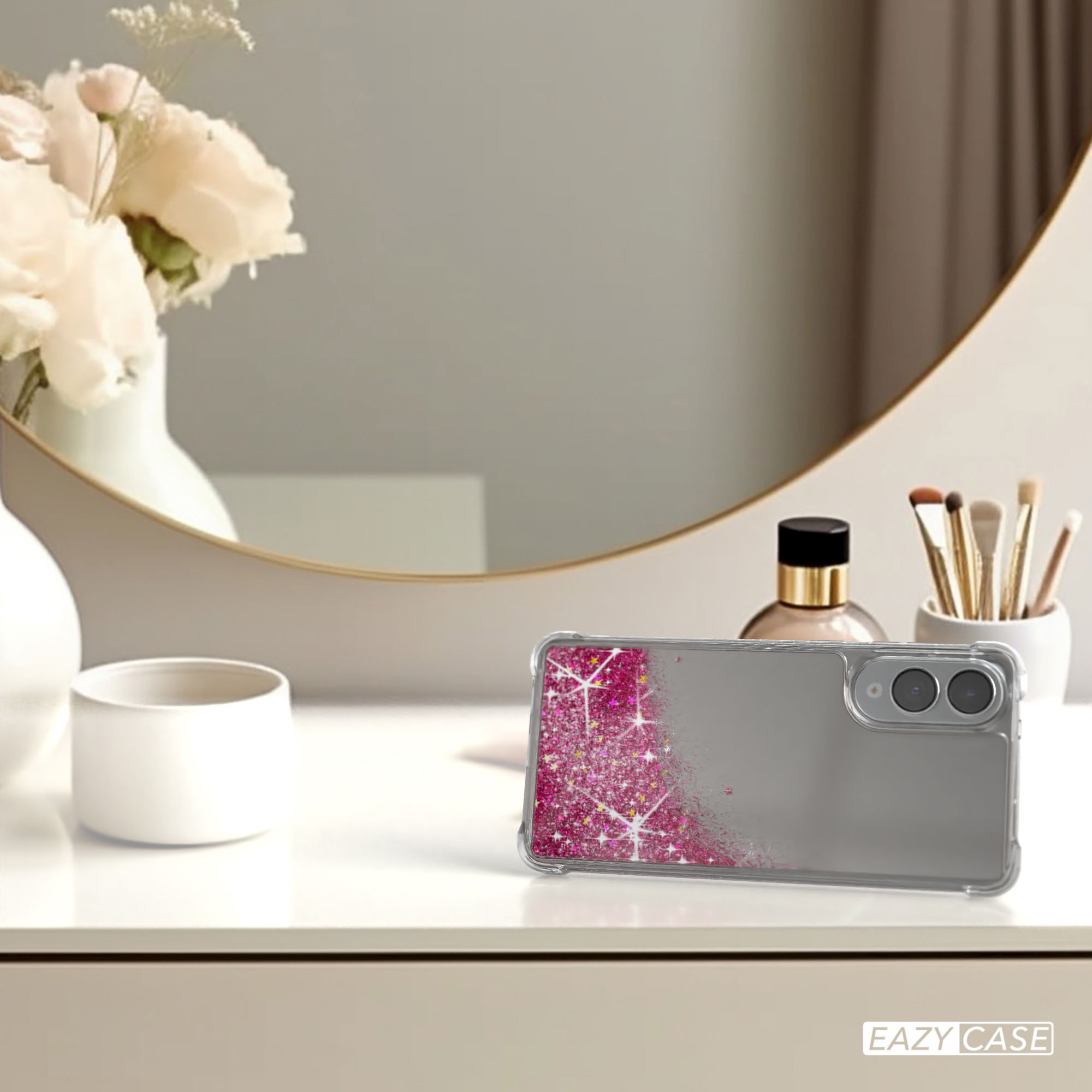 Handyhülle mit rosa Glitzer auf einem Tisch. Ein Spiegel, Blumen und Make-up-Pinsel sind im Hintergrund.