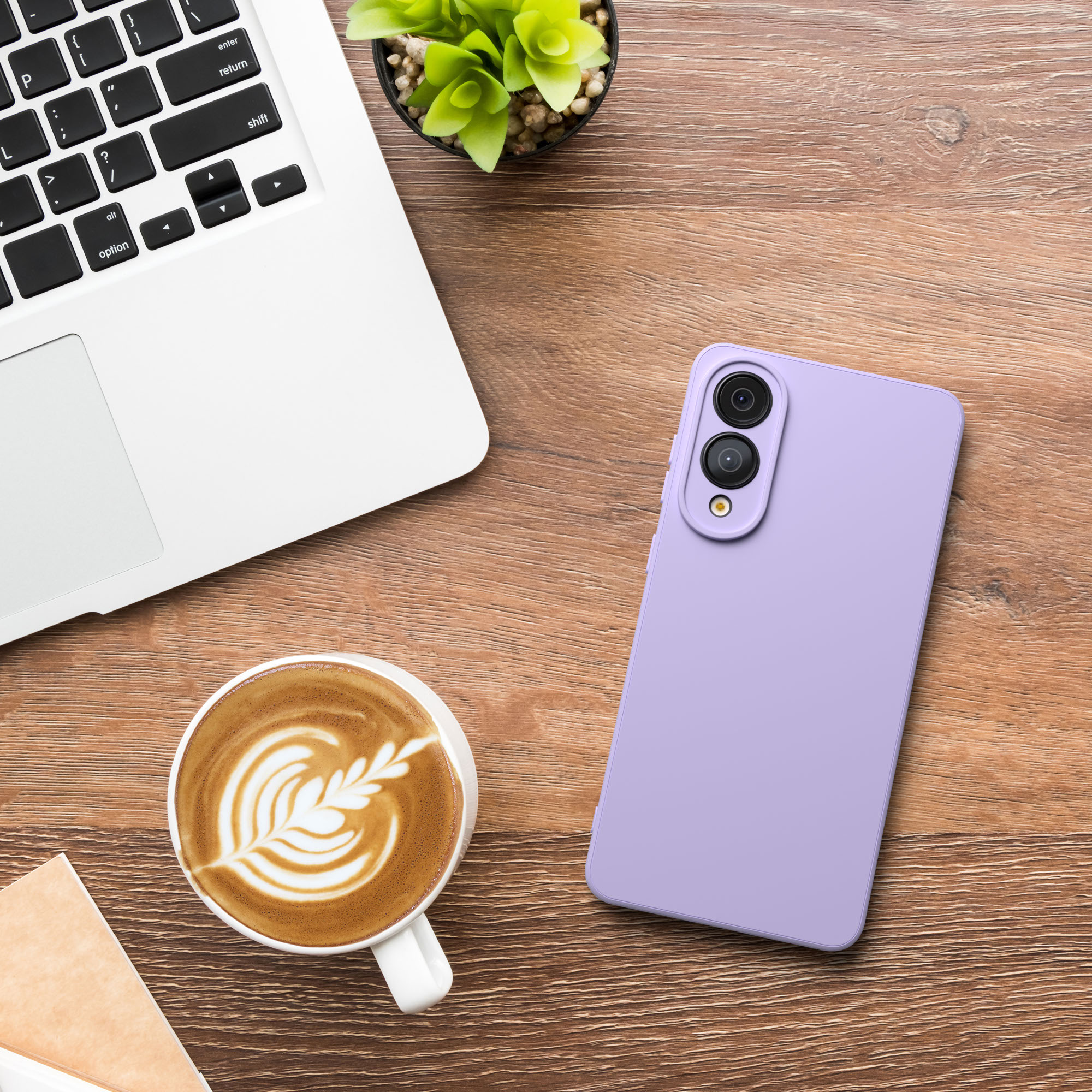 Ein Laptop, eine Kaffeetasse und ein lila Telefon auf einem Holztisch. Es gibt auch eine kleine Pflanze in einem Topf.