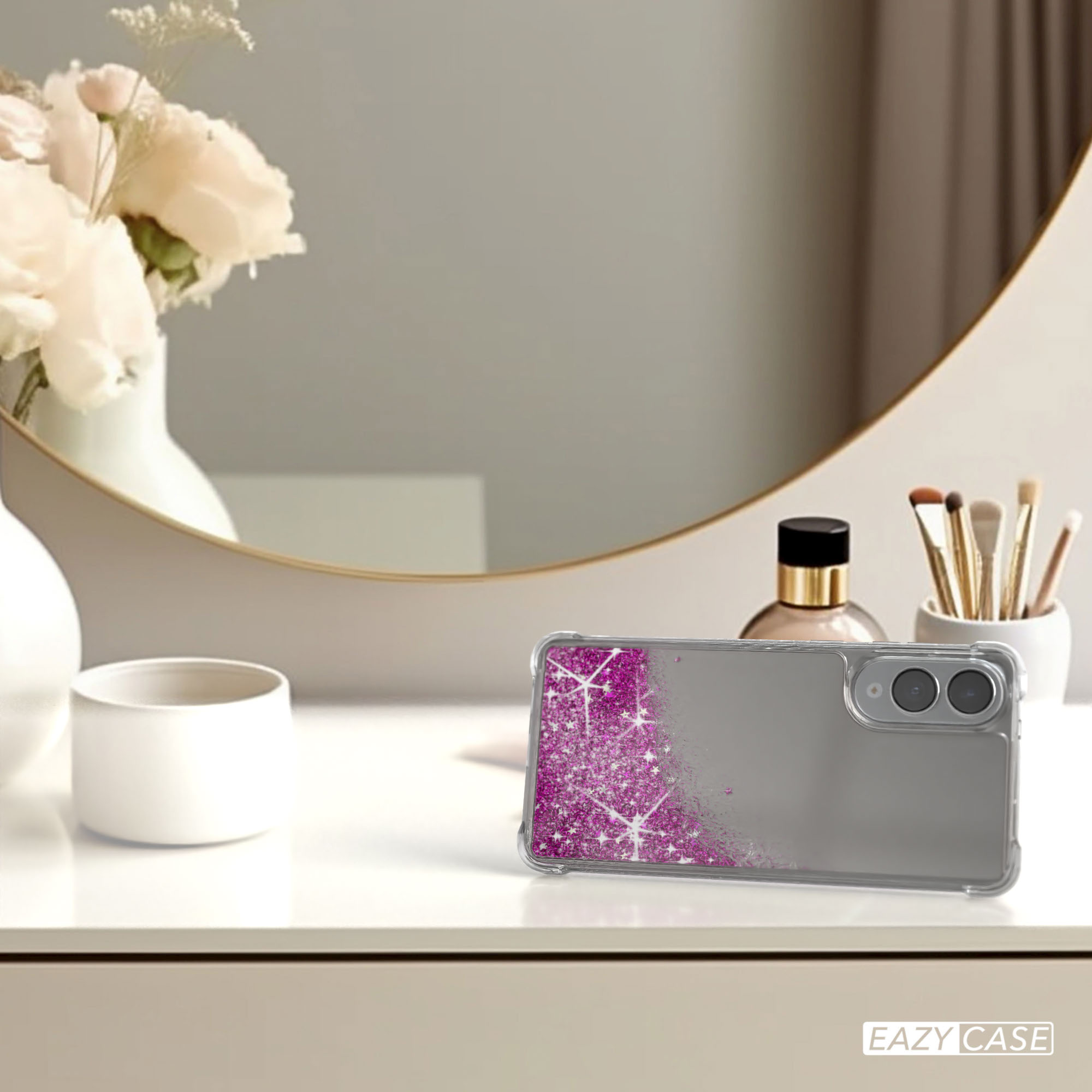 Eine Handyhülle mit rosa Glitzer und grauem Hintergrund liegt auf einem weißen Tisch. Blumen, Spiegel und Make-up sind ebenfalls sichtbar.