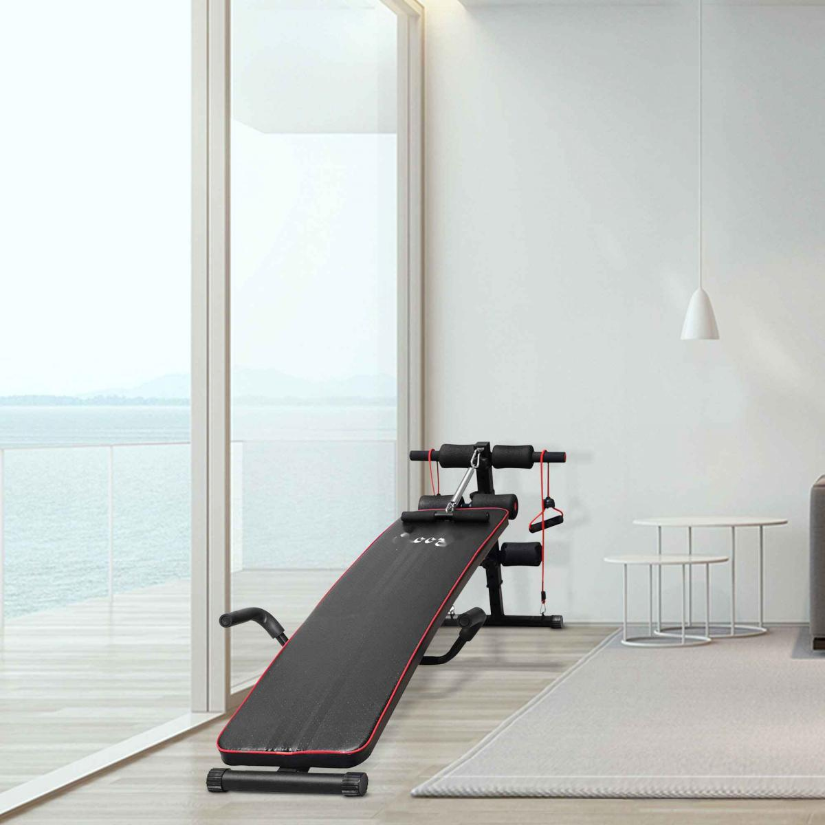 Eine schwarz-rote Trainingsbank steht in einem hellen Raum. Ein großes Fenster überblickt das Meer. Eine weiße Lampe hängt von der Decke.