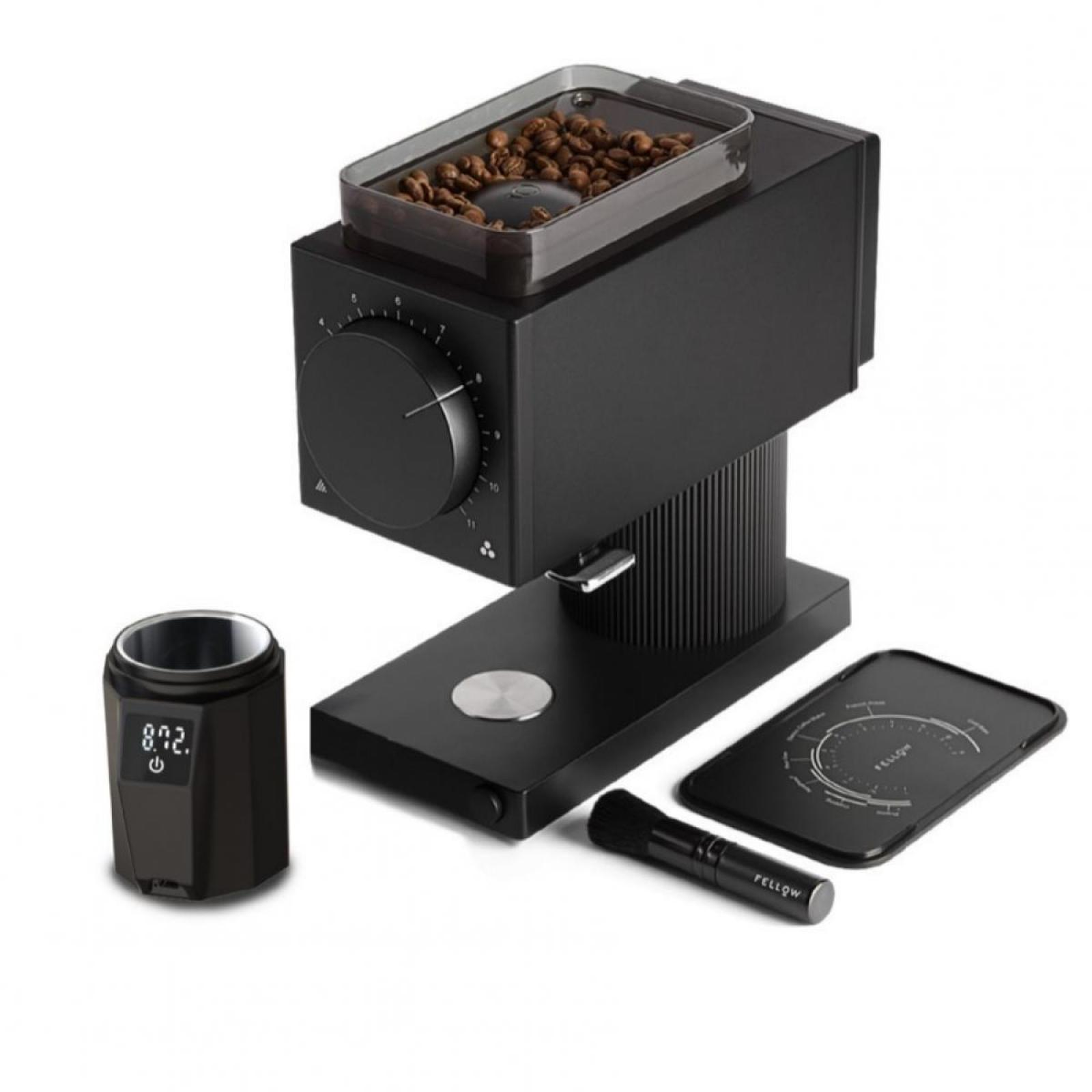 Schwarze Kaffeemühle mit Zubehör: Becher, Bürste und Platte. Bohnen liegen in einem Behälter.