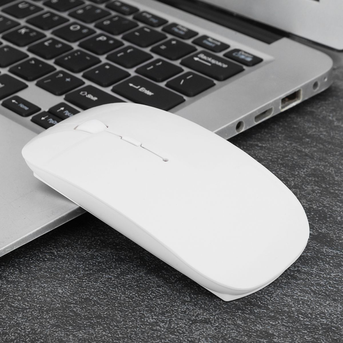 Eine weiße kabellose Maus liegt auf einer Laptop-Tastatur. Die Tastatur ist schwarz und silbern. Der Hintergrund ist eine dunkelgraue Oberfläche.