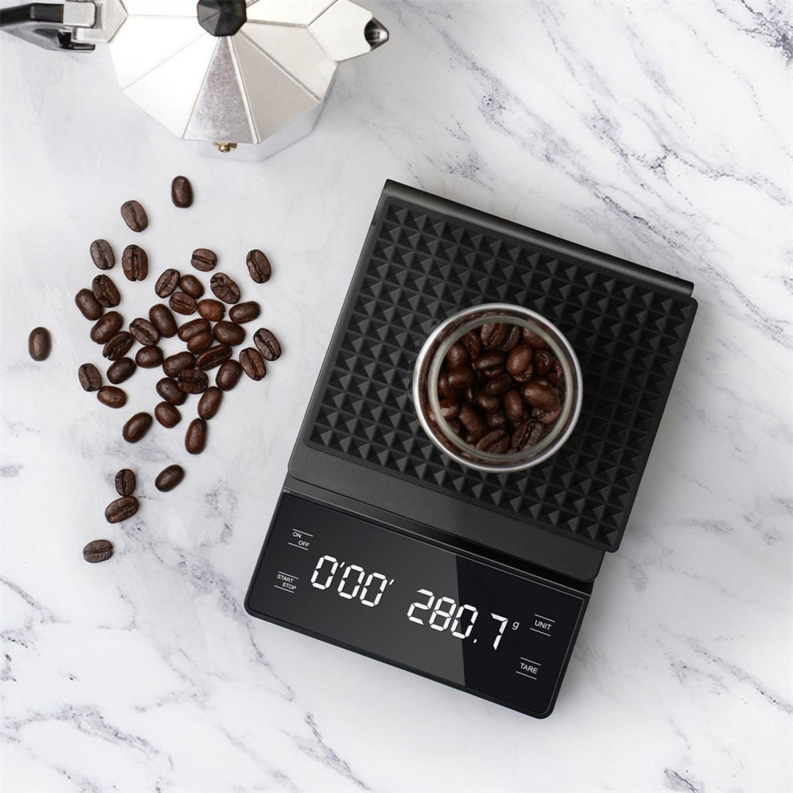 Kaffeebohnen auf einer Waage, Espressomaschine und verstreute Bohnen auf Marmor. Die Waage zeigt 280,7 g.