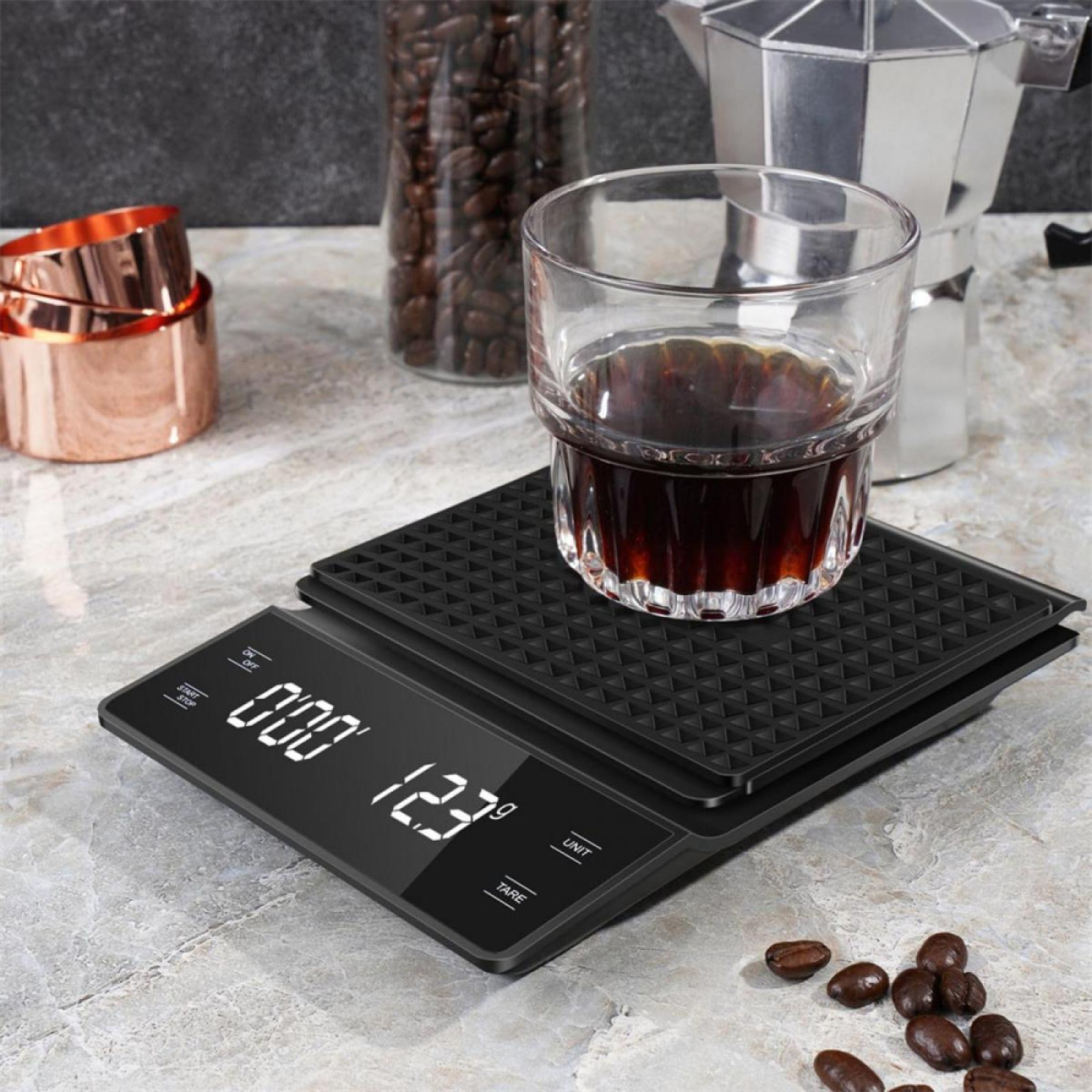 Eine Kaffeewaage mit einem Glas Kaffee, Messbechern, Kaffeebohnen und einer Kaffeemaschine im Hintergrund.