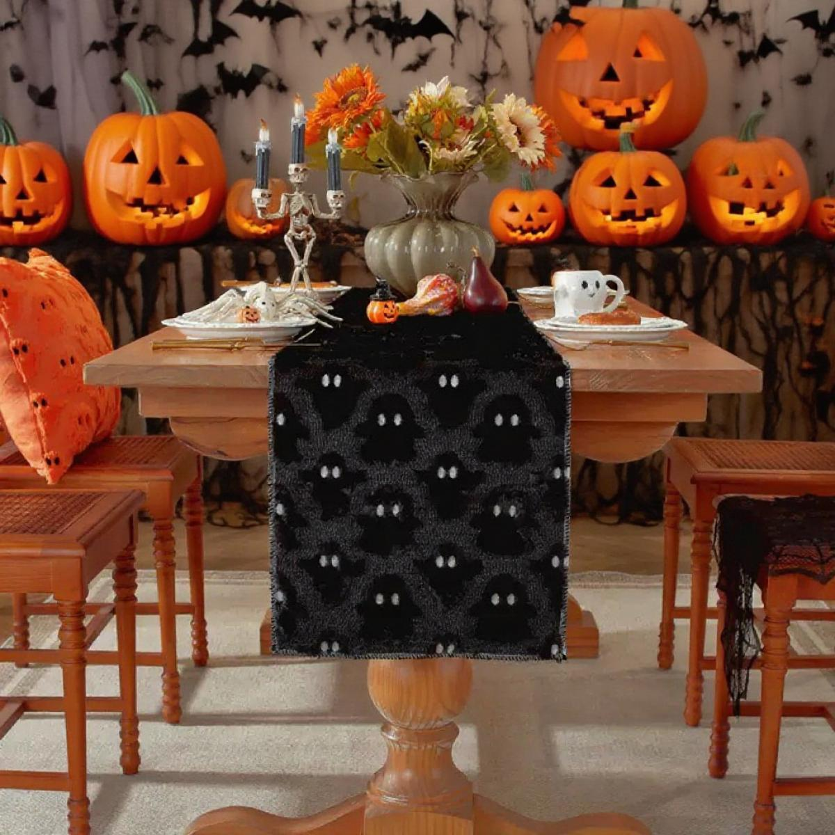 Halloween-Tischdeko. Kürbisse, Blumen und ein Geisterläufer auf einem Holztisch. Kerzen, ein Skelett und eine Tasse.