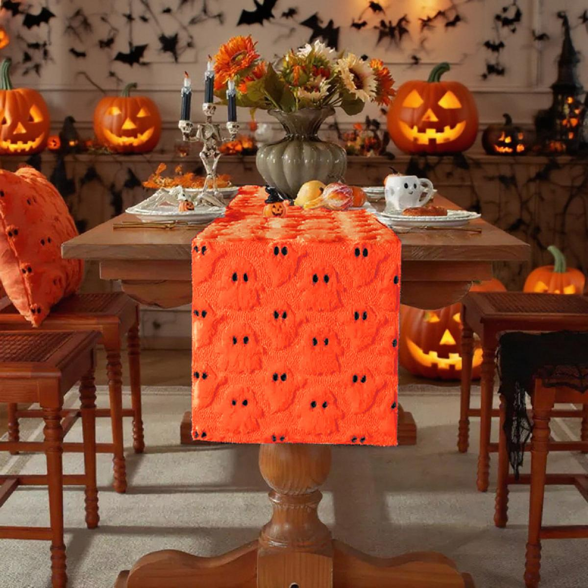 Eine Halloween-Tischdekoration mit Kürbislaternen, einem orangefarbenen Tischläufer mit Geistermuster, Blumen und Kerzen. Stühle und ein Kürbis vervollständigen die Szene.