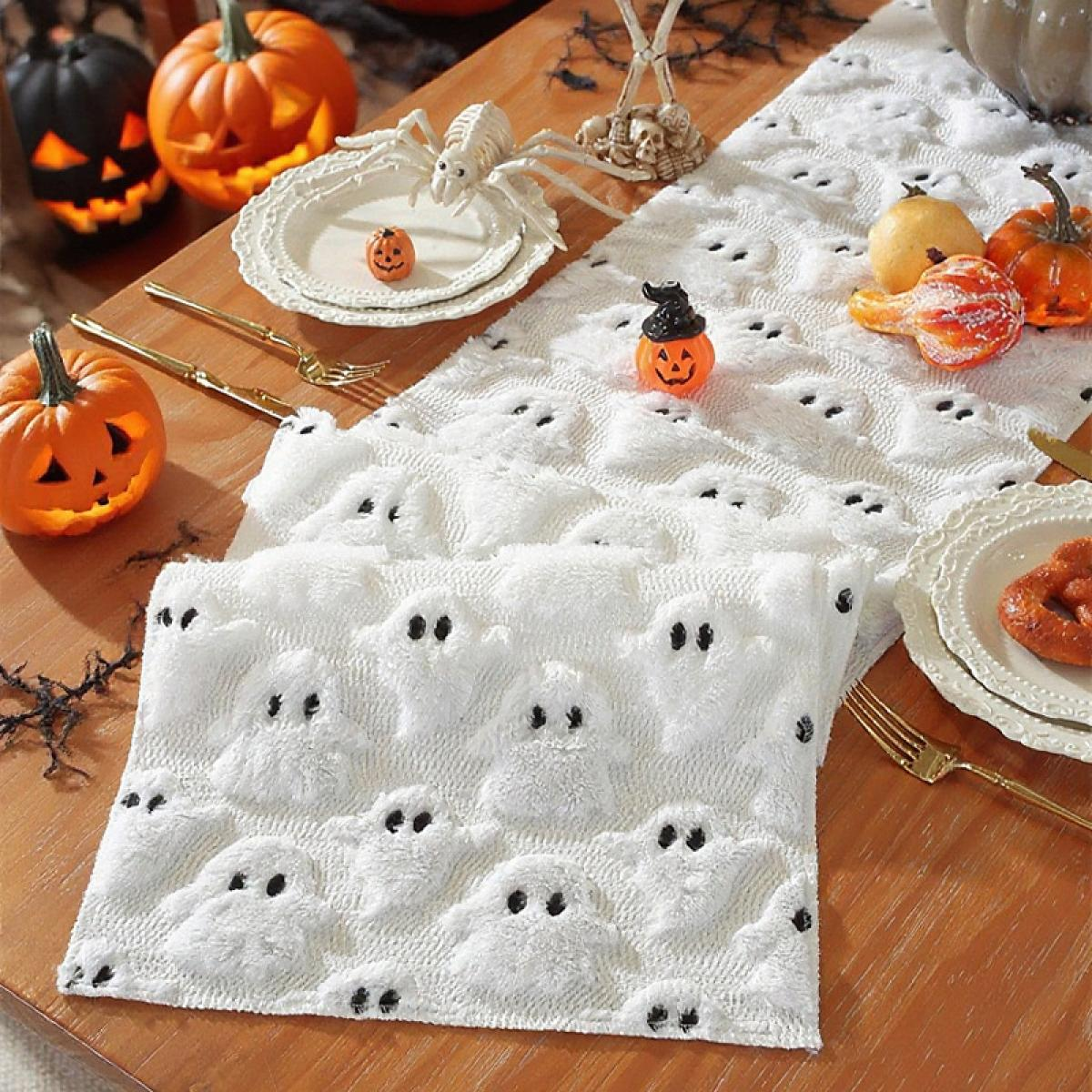 Halloween-Tischdeko. Kürbisse, Geistermuster-Tuch, Spinne, Teller und Besteck auf einem Holztisch.