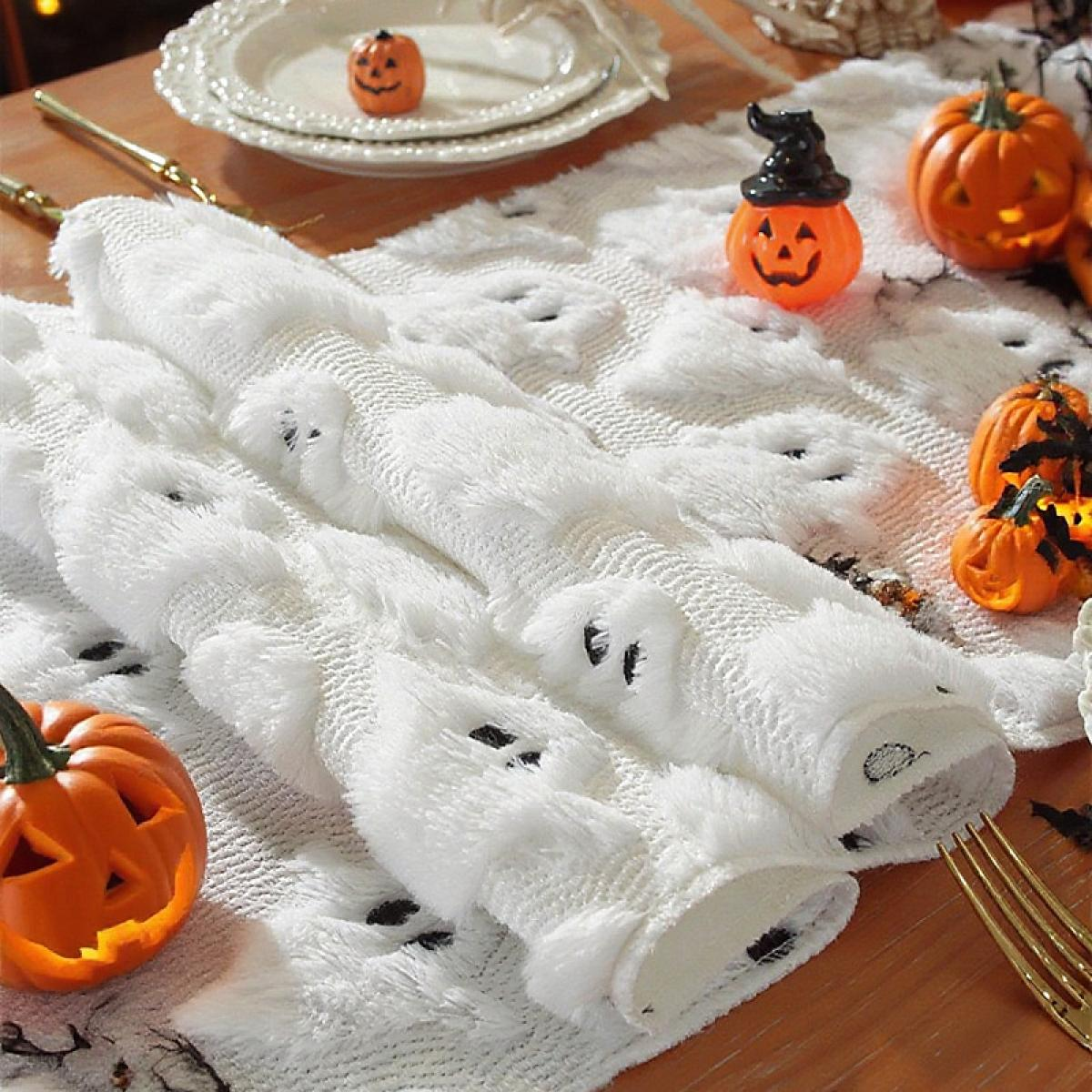 Halloween-Tischdekoration. Weiße, geisterförmige Läufer, orangefarbene Kürbisse, Teller und eine Gabel. Festlich und dekorativ für den Feiertag.