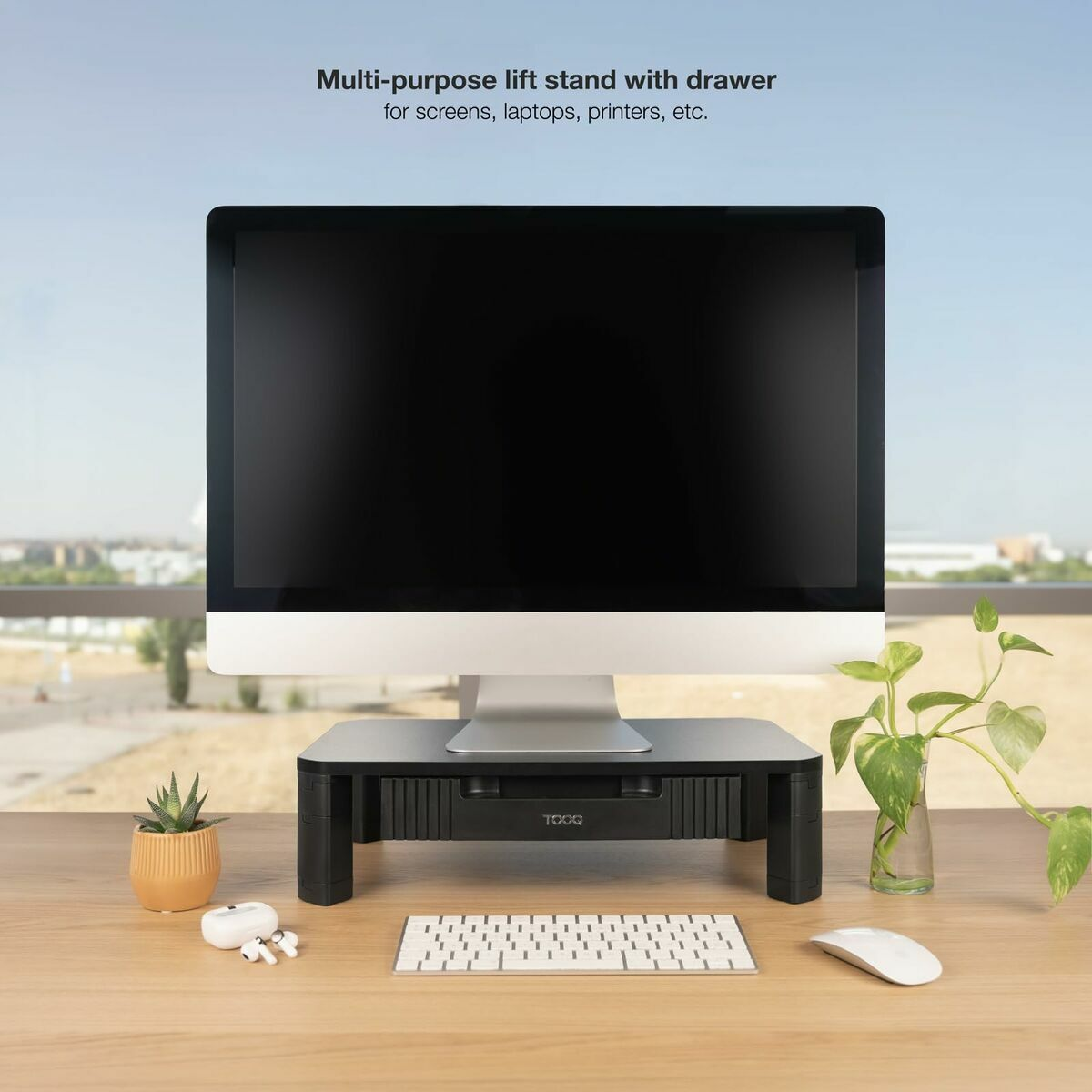 Un monitor per computer è su un supporto nero con un cassetto. Tastiera, mouse e piccole piante sono sulla scrivania di legno.