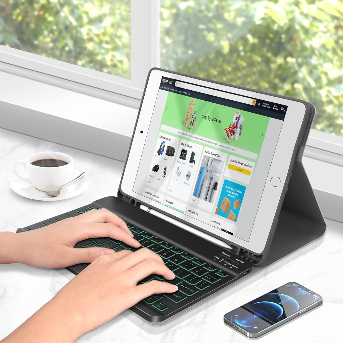 Eine Person tippt auf einer Tastatur, die an ein Tablet angeschlossen ist. Ein Smartphone und eine Tasse Kaffee stehen ebenfalls auf dem Tisch.