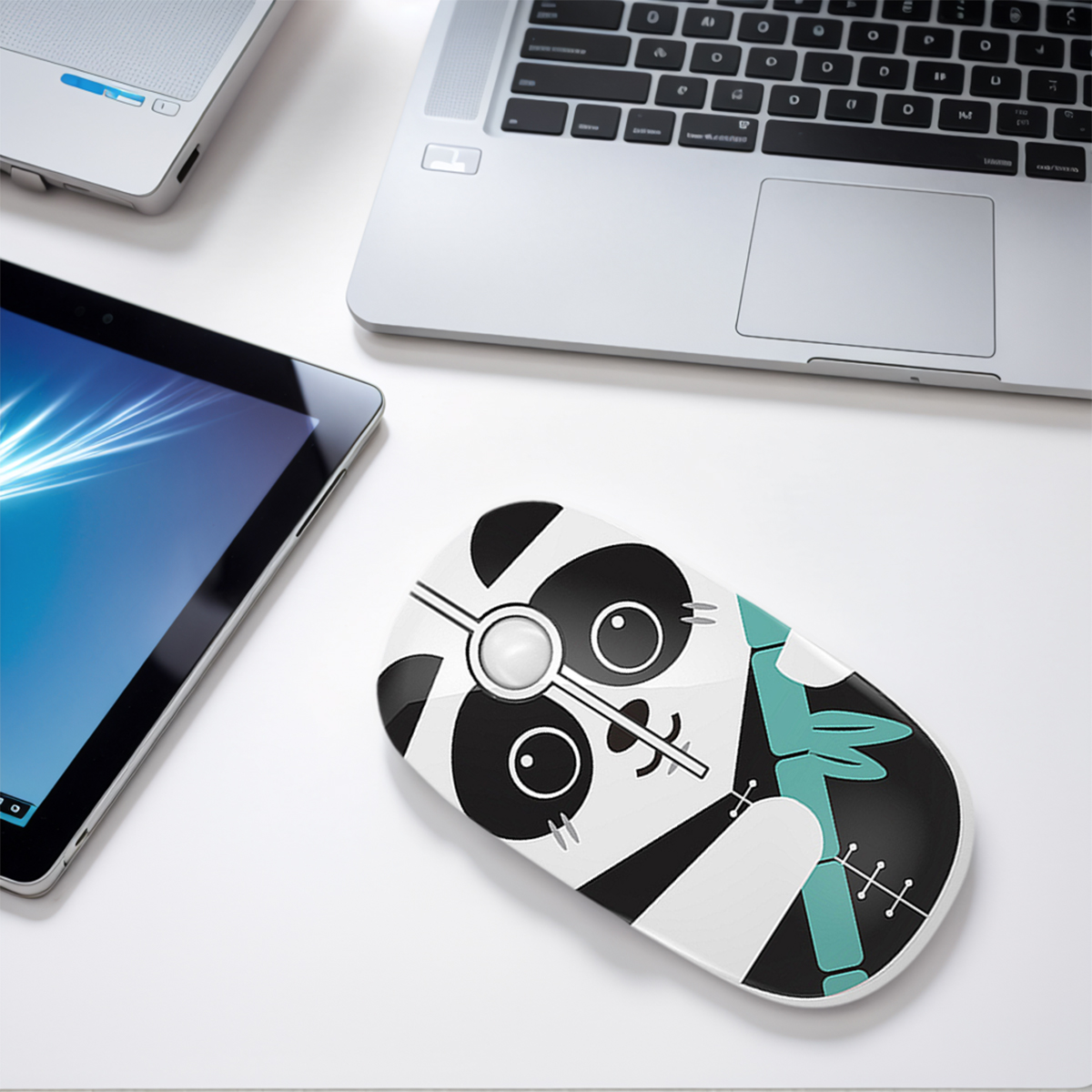Eine Computermaus mit Panda-Design, neben einem Laptop und einem Tablet, alles auf einer weißen Oberfläche. Die Maus hat Schwarz-Weiß-Farben.