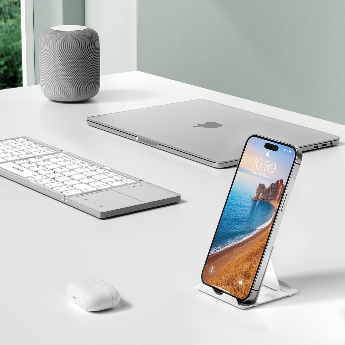 Ein Schreibtisch mit Laptop, Telefon, Tastatur, Lautsprecher und Ohrhörern. Das Telefon zeigt ein Strandbild. Alles ist grau und weiß.