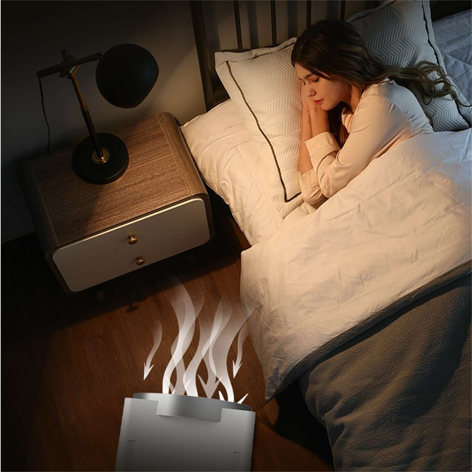 Eine Frau schläft im Bett. Eine Lampe und ein Nachttisch stehen daneben. Ein Luftreiniger steht auf dem Boden, mit aufsteigendem Dampf.