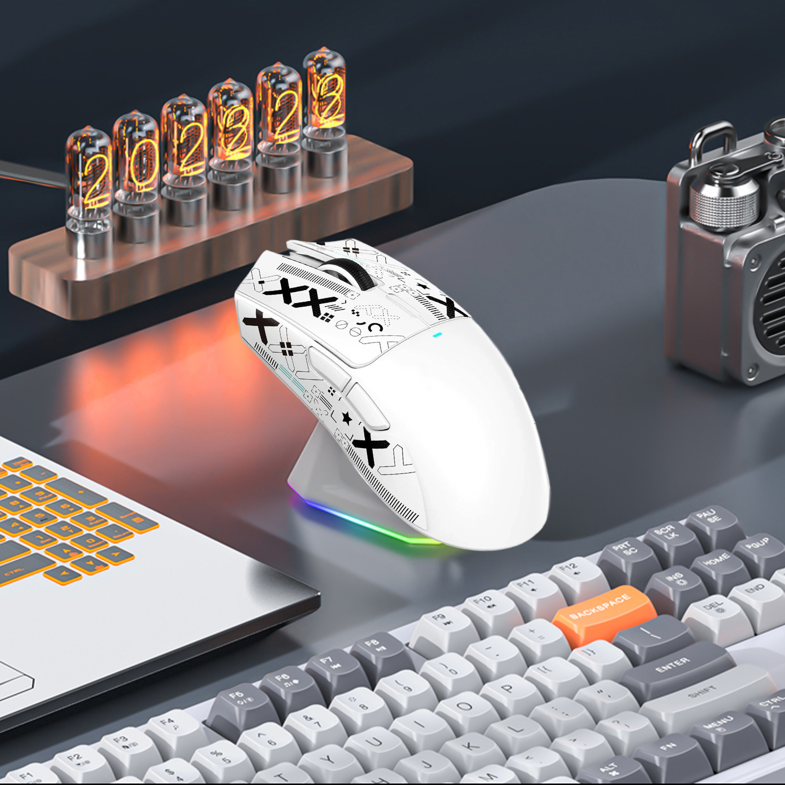 Weiße Maus mit schwarzen Akzenten auf einem Ladeständer. Dahinter eine Tastatur und Röhren.
