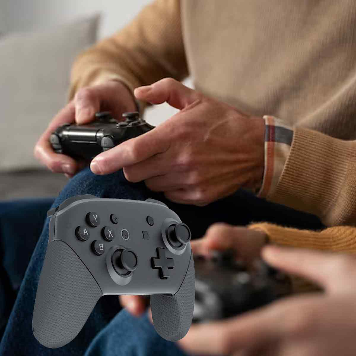 Eine Person hält einen grauen Gamecontroller im Vordergrund. Eine andere Person hält einen schwarzen Controller im Hintergrund.